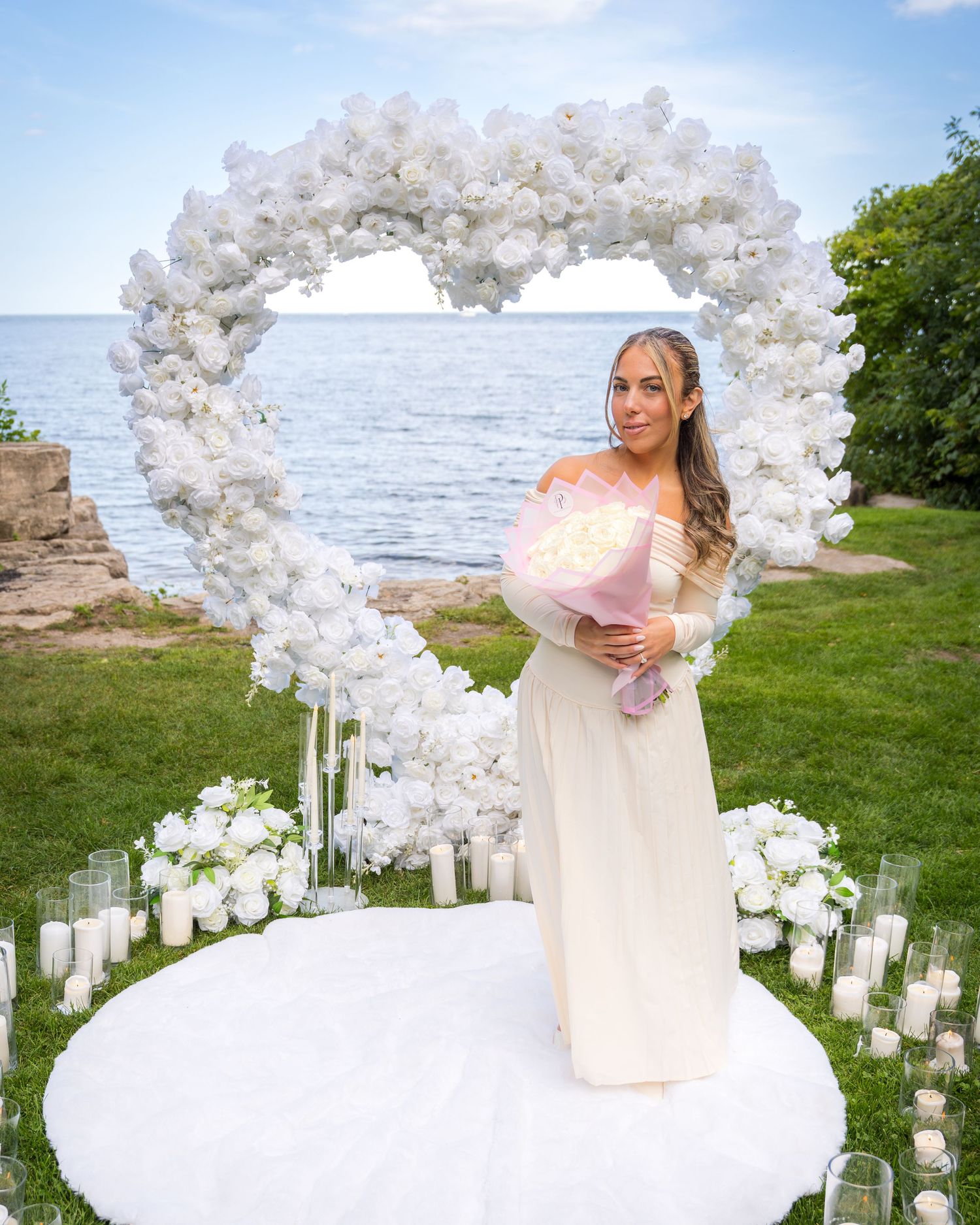 A romantic seaside proposal scene with white floral decorations and candle-lined pathway.