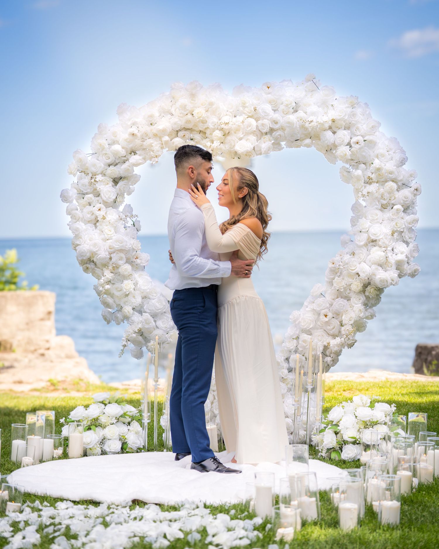 Elegant oceanside wedding ceremony site decorated with white floral arch and candles.