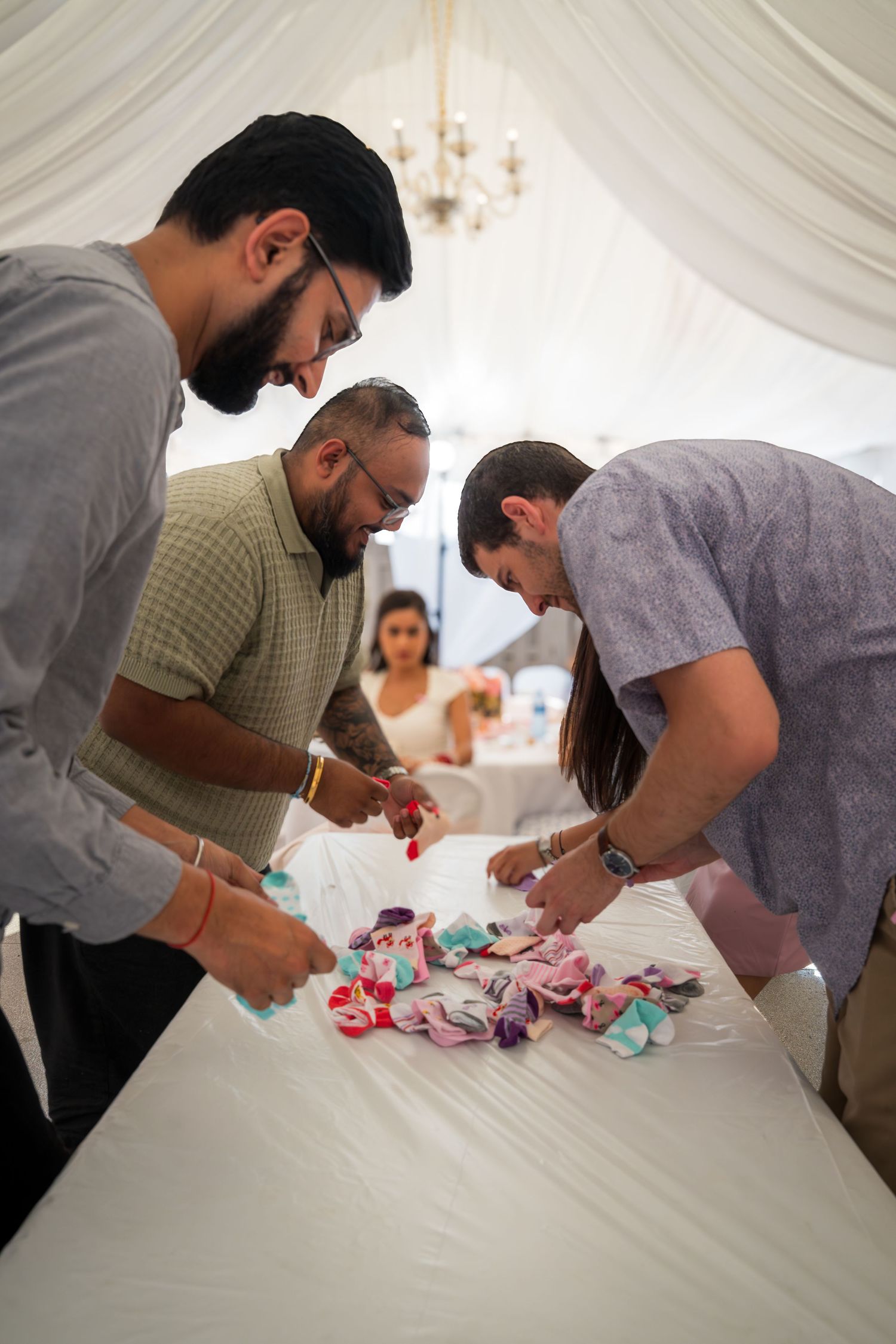 Party guests participating in a baby shower game on a white table.