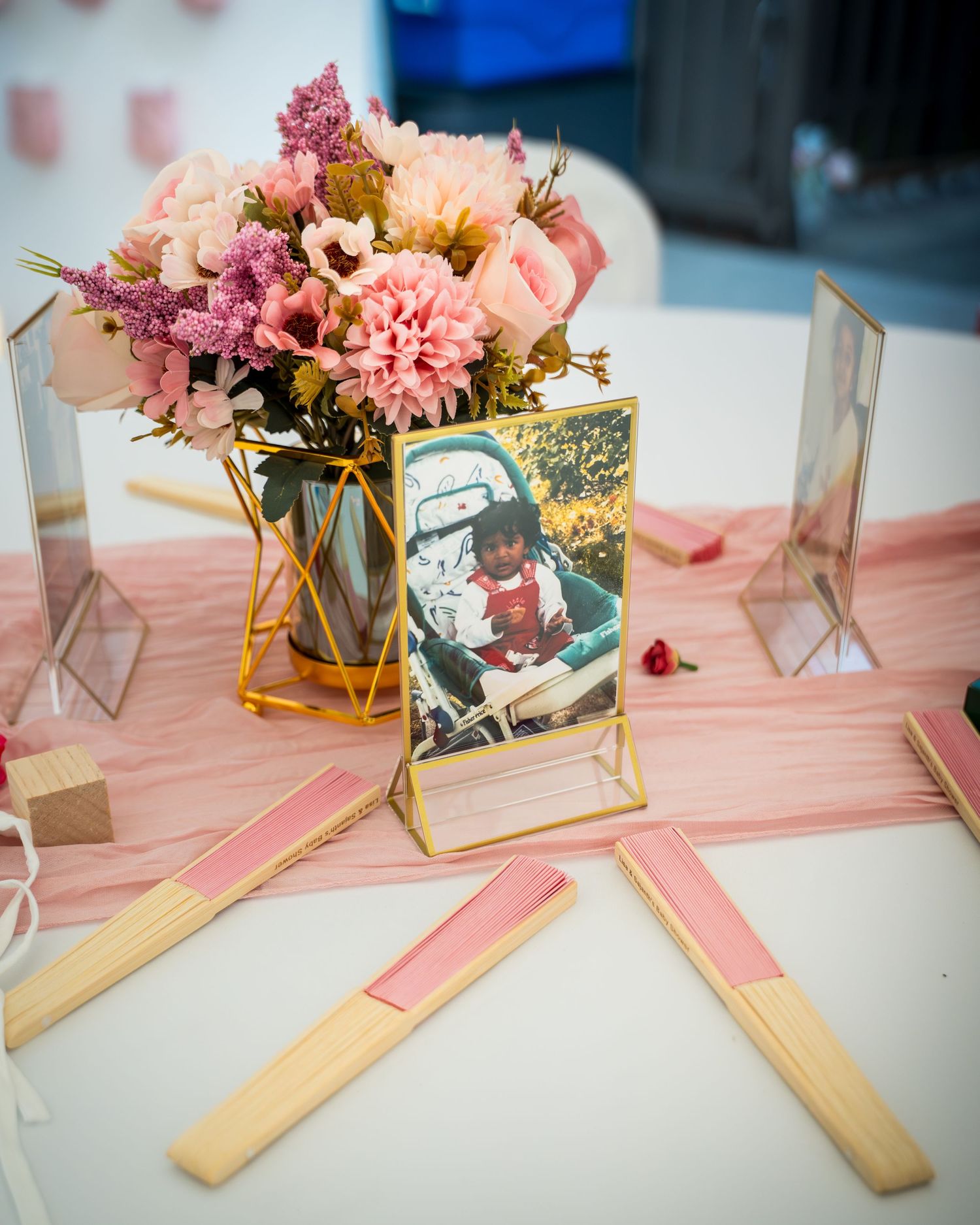 Decorative table setup with pink flowers in gold geometric vases and framed photos.