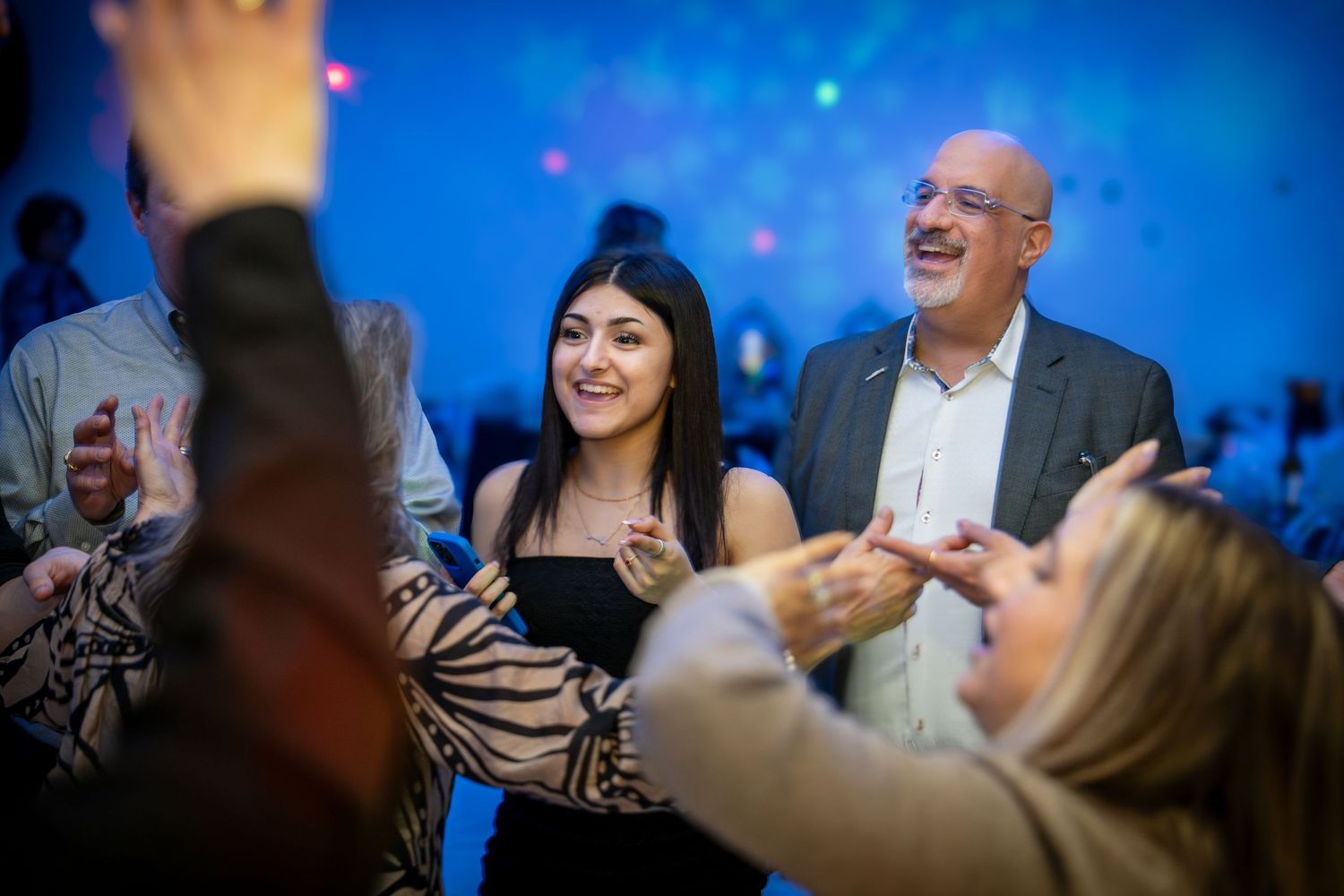 Joyful celebration with people dancing and laughing under blue party lights.