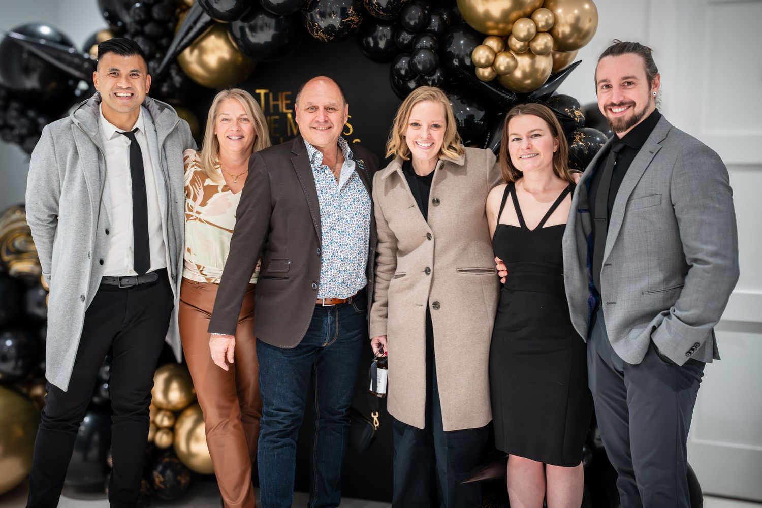 Group photo at formal event with gold balloon decorations and black backdrop.