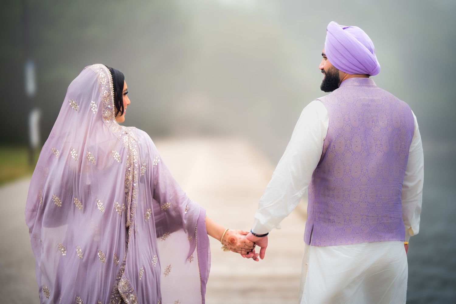 Couple in coordinated traditional attire walking hand in hand on a misty day.