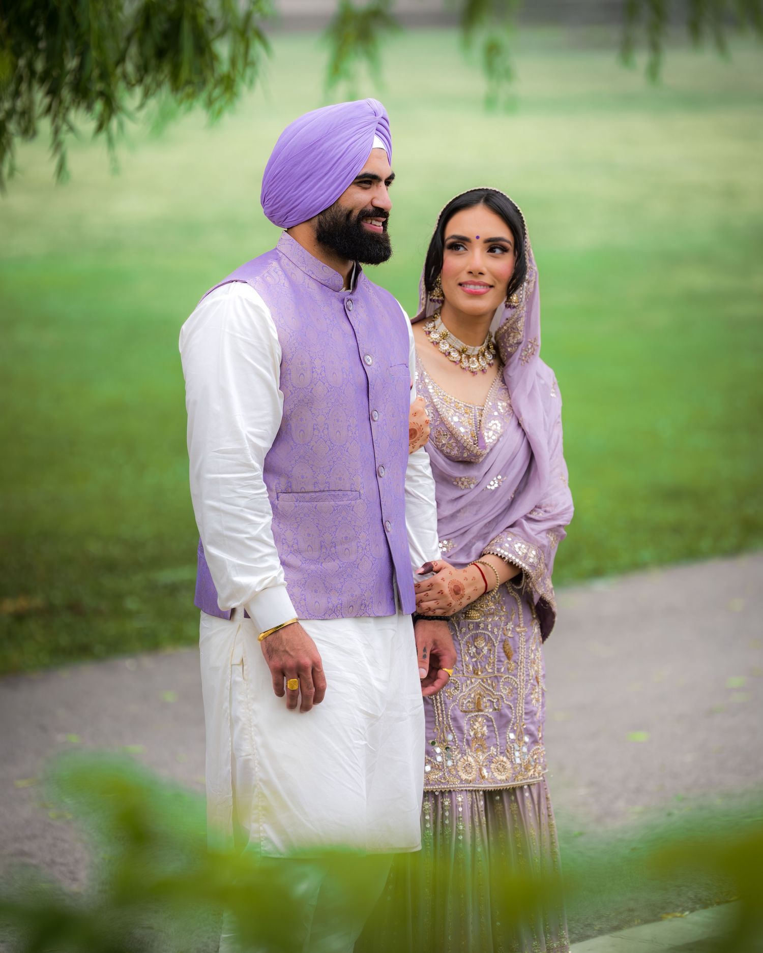 A romantic couple in coordinated purple attire shares a tender moment in a lush park setting.