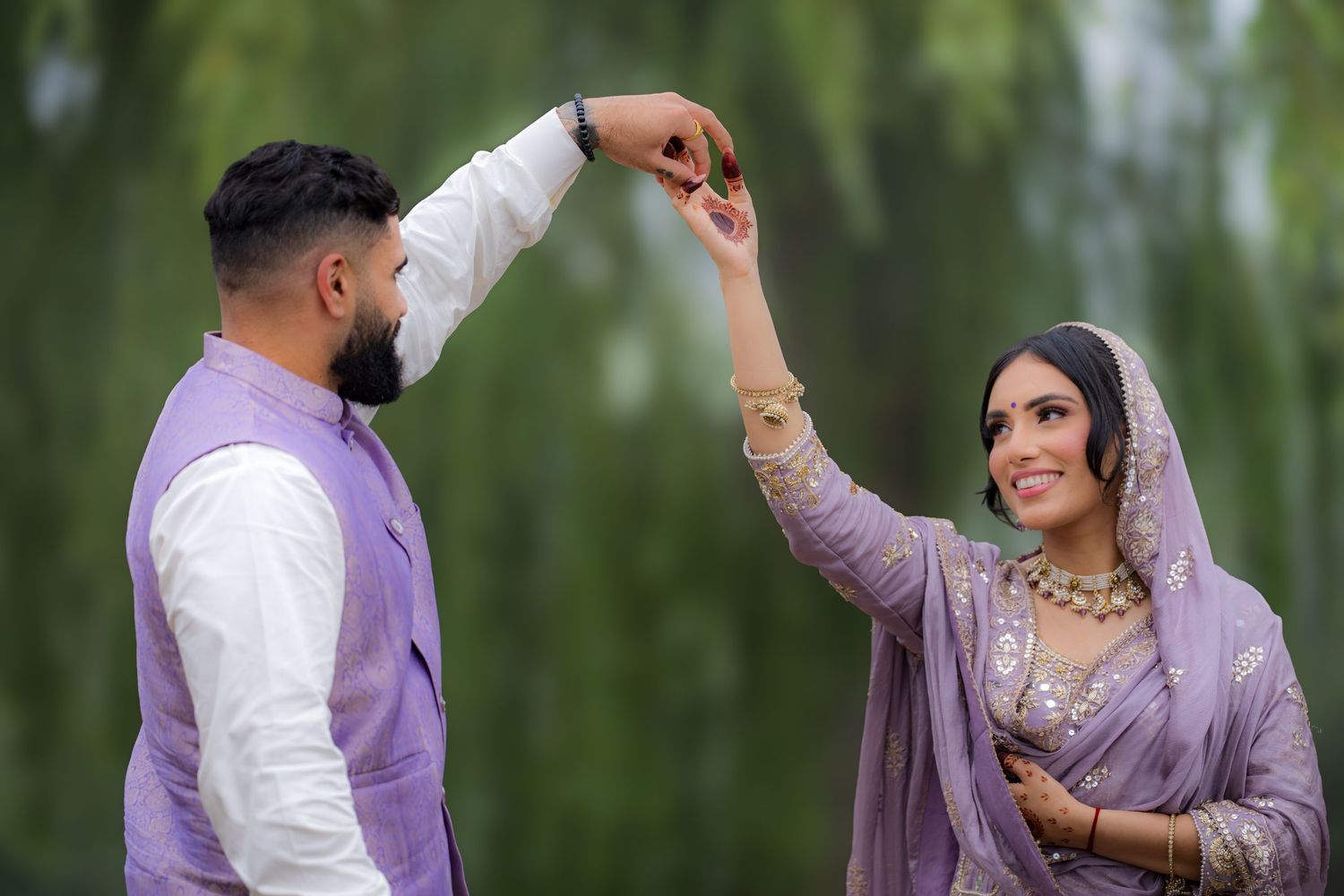 A couple in traditional Punjabi attire share a dance moment under weeping willow trees.