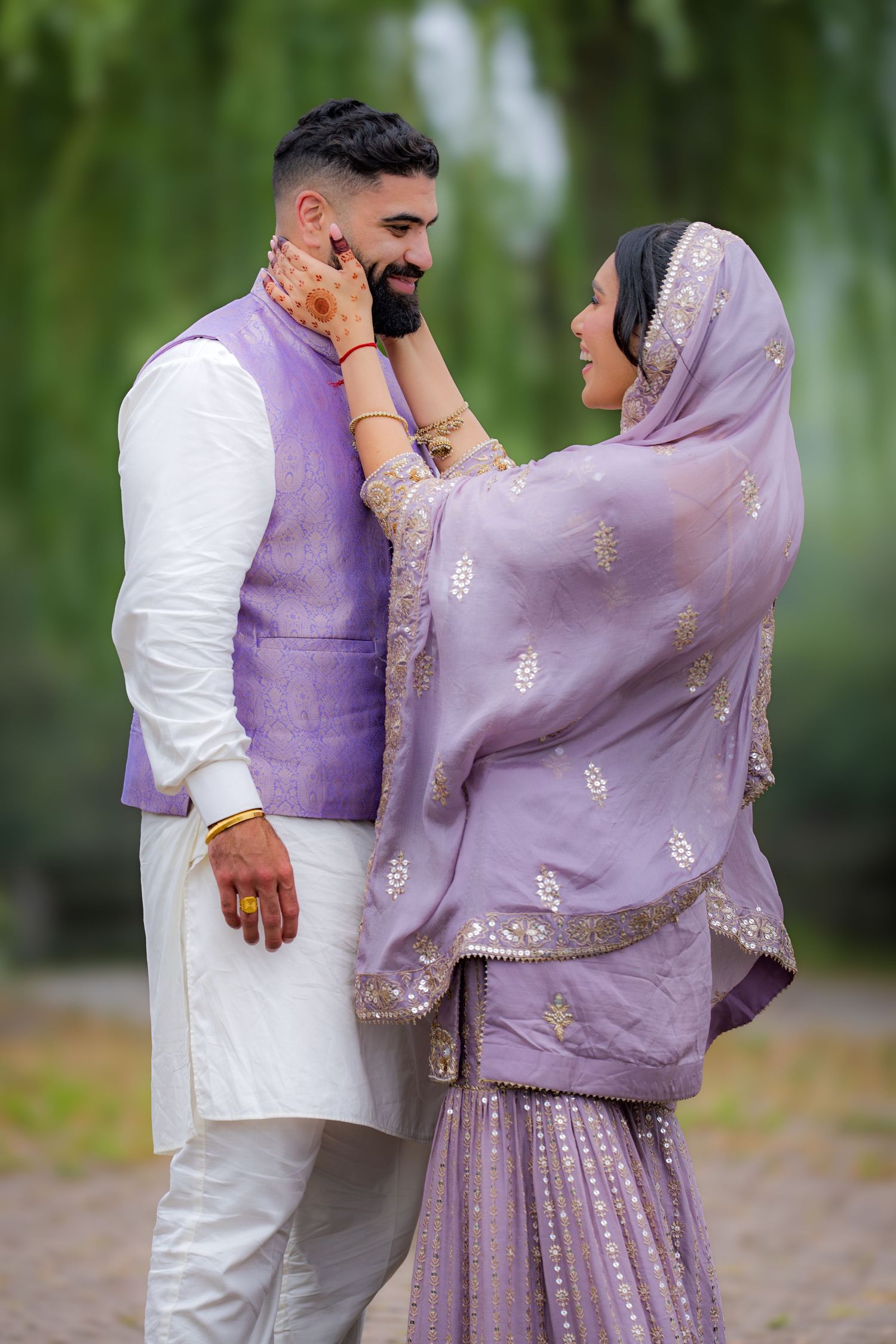 A romantic couple in traditional Punjabi dress shares a playful moment under willow trees.