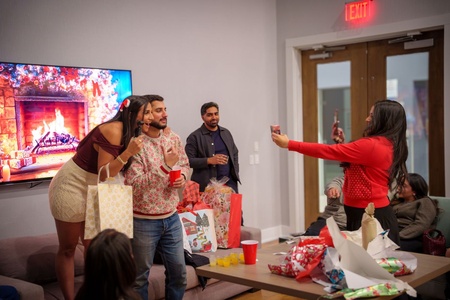 People enjoying a lively holiday gathering in living room with TV and gift exchange.