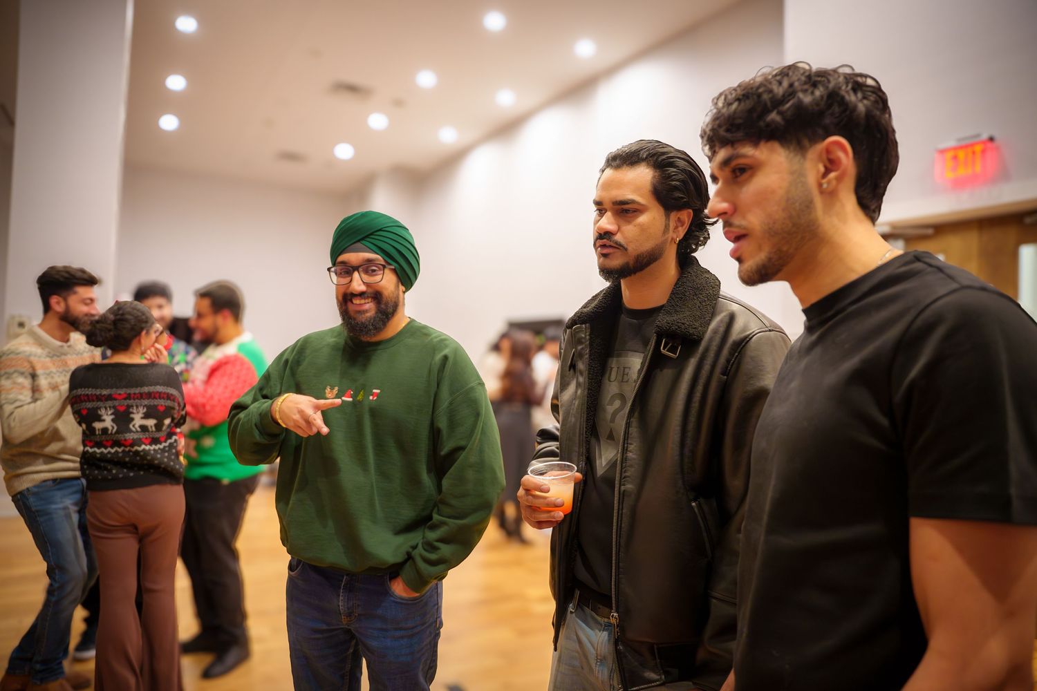 A group stands together in casual attire having a discussion in an indoor space with recessed lighting.