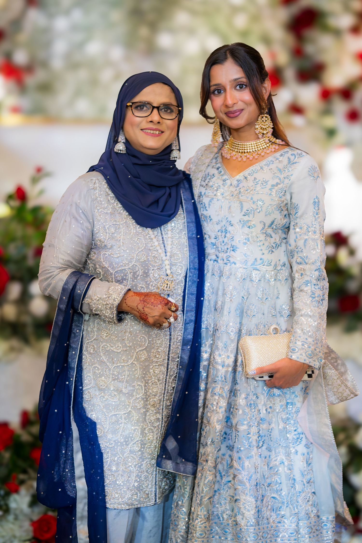Wedding guests in elegant blue and silver traditional outfits pose together against floral backdrop.