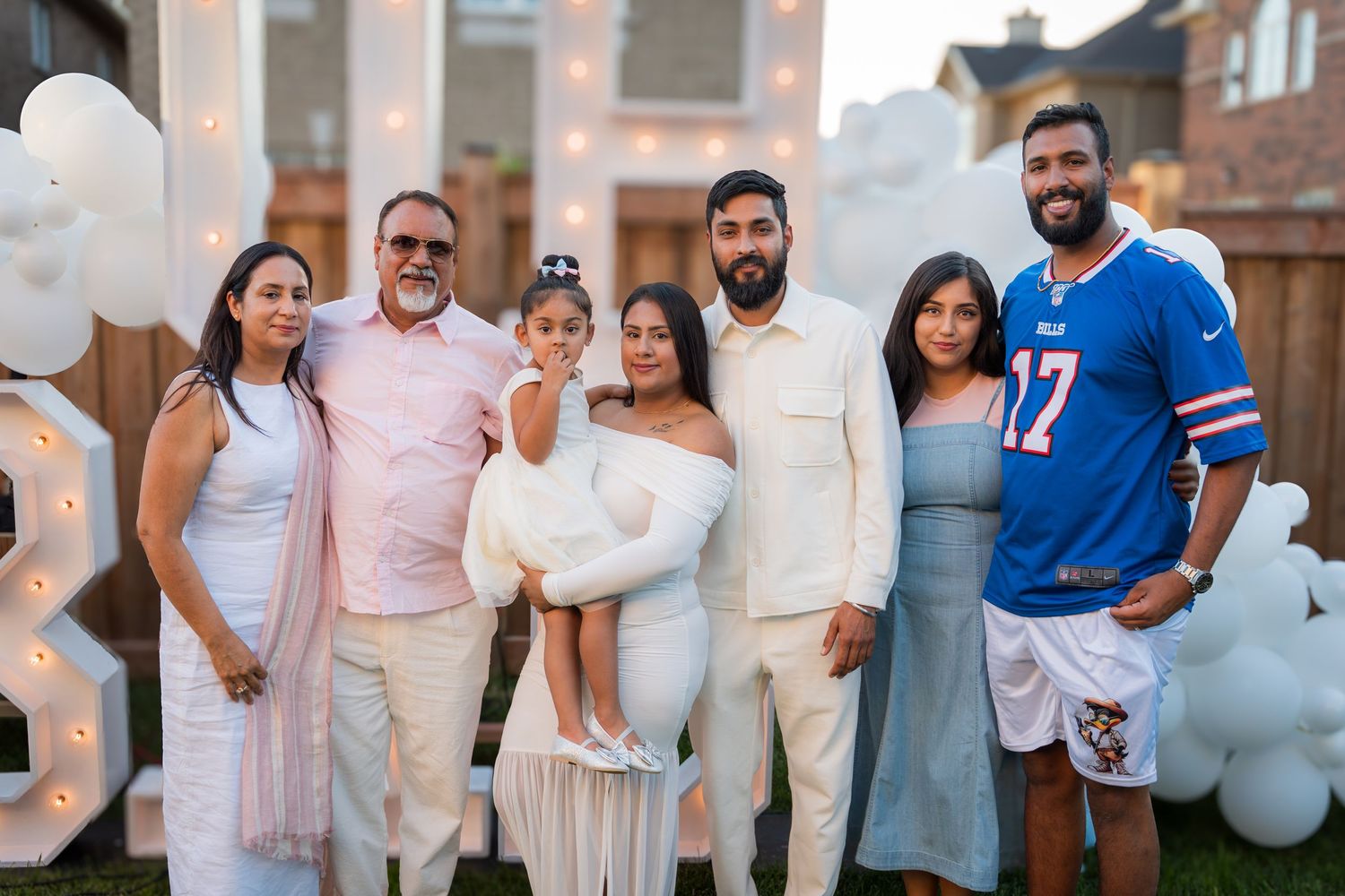 Family of seven poses together in front of white balloon arch and marquee letters at a gender reveal.