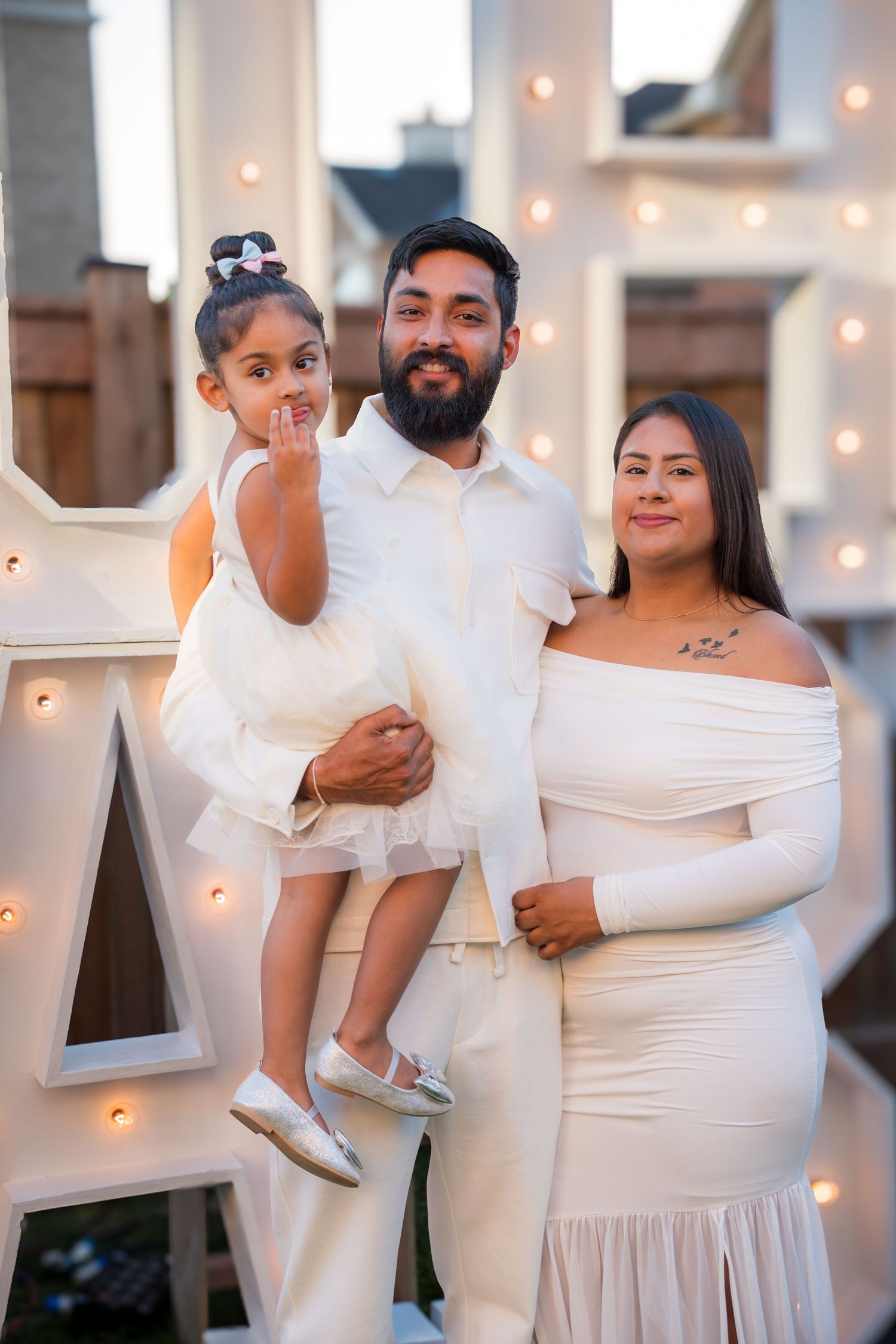 Smiling family of three in matching white outfits posing at an outdoor baby shower celebration.