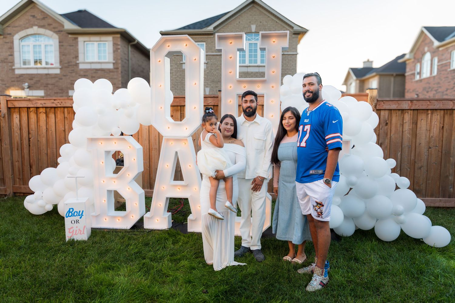Group of four people posing in front of OH BABY marquee letters surrounded by white balloon garland.