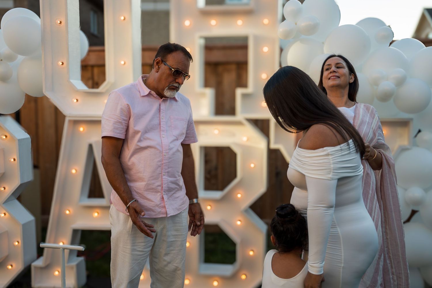 Family gathering near illuminated BABY marquee letters at an outdoor baby shower event at dusk.