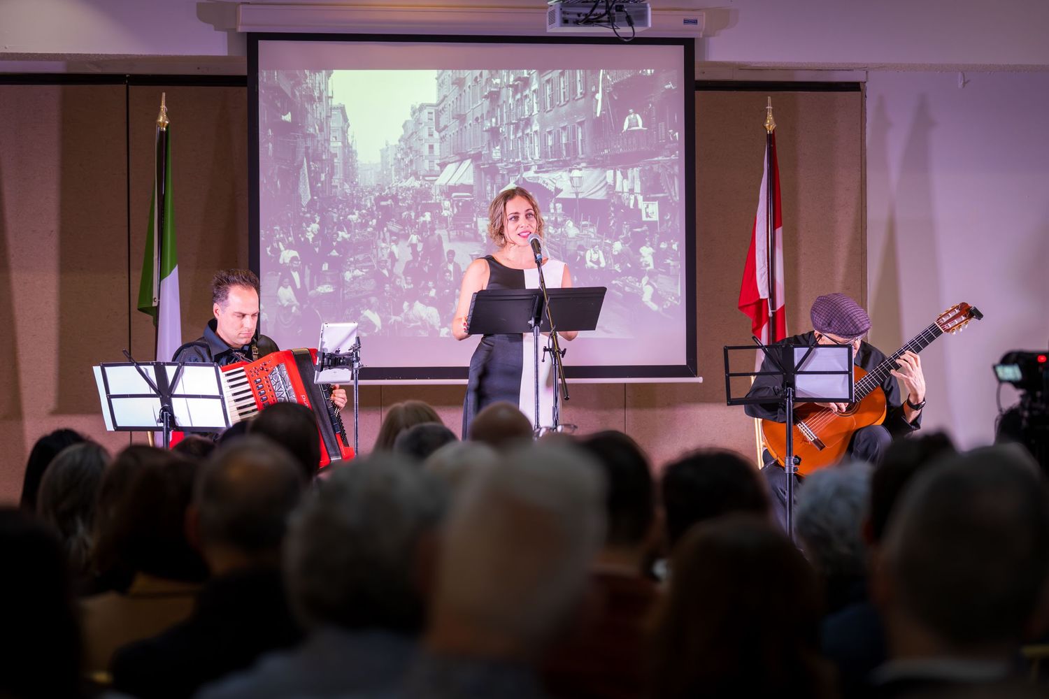 Live musical performance with accordion and guitar players flanking a female vocalist on a dimly lit stage.