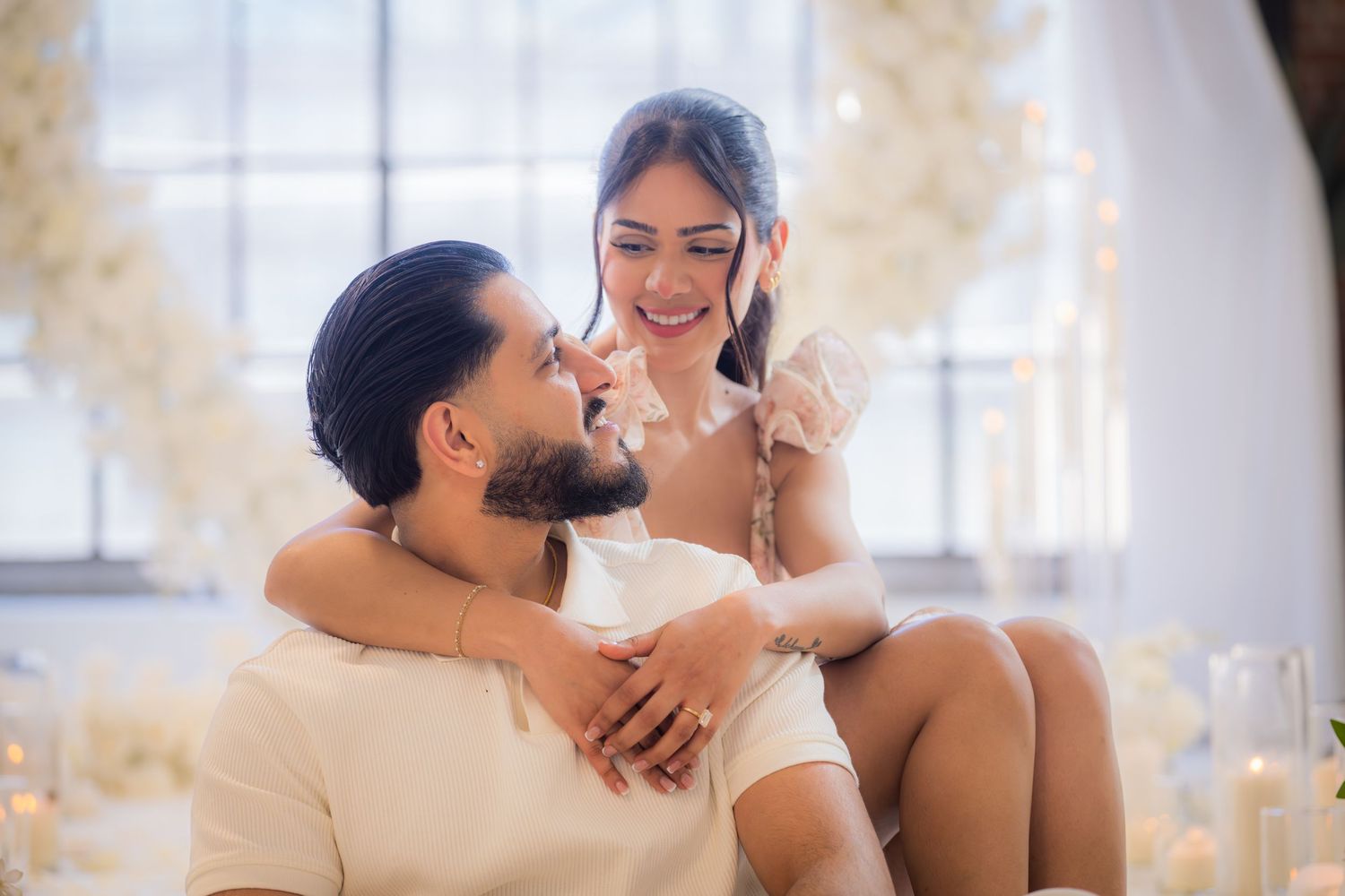 Happy couple sitting together surrounded by white flowers and candles in a romantic setting.