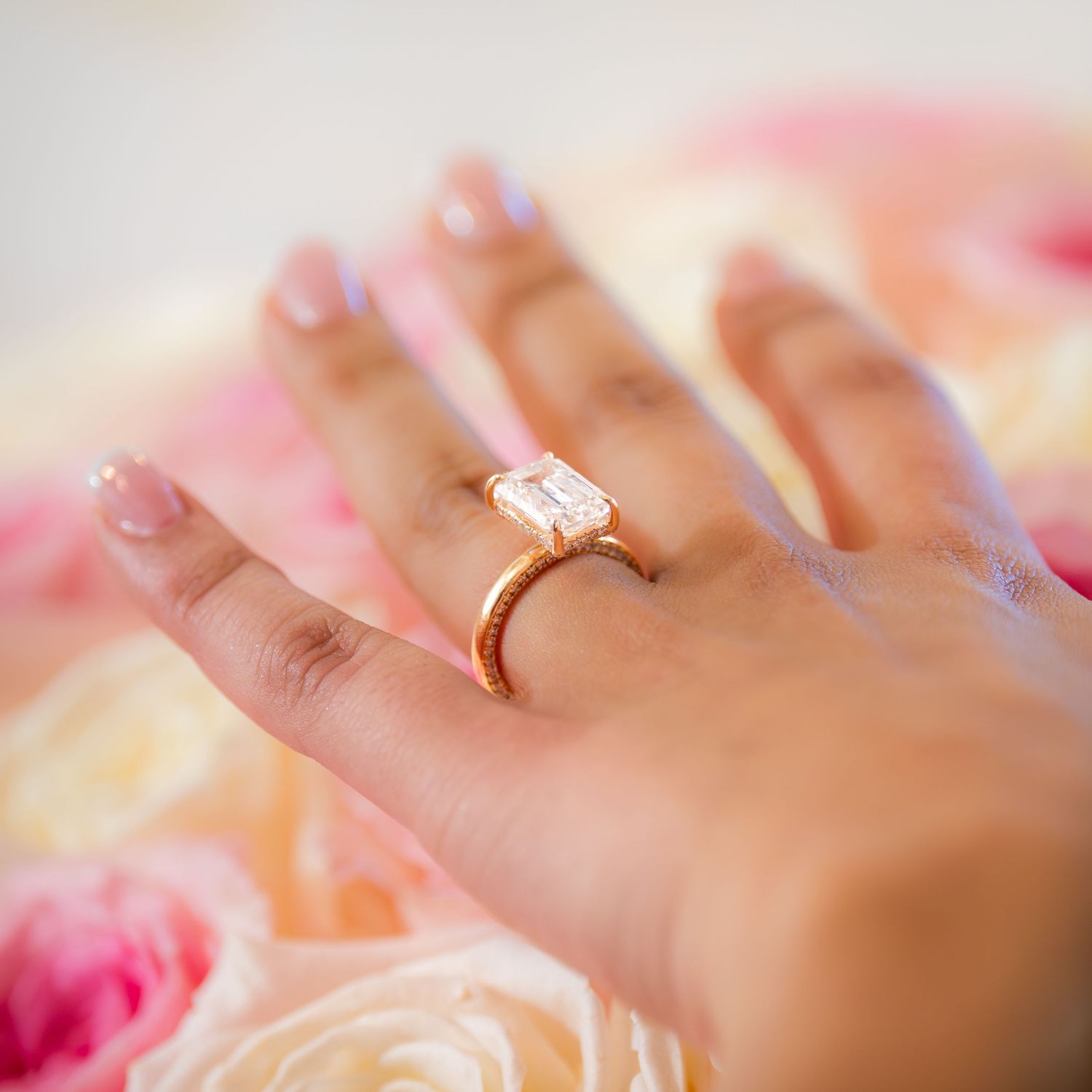 Emerald cut diamond engagement ring on rose gold band held over pink roses.