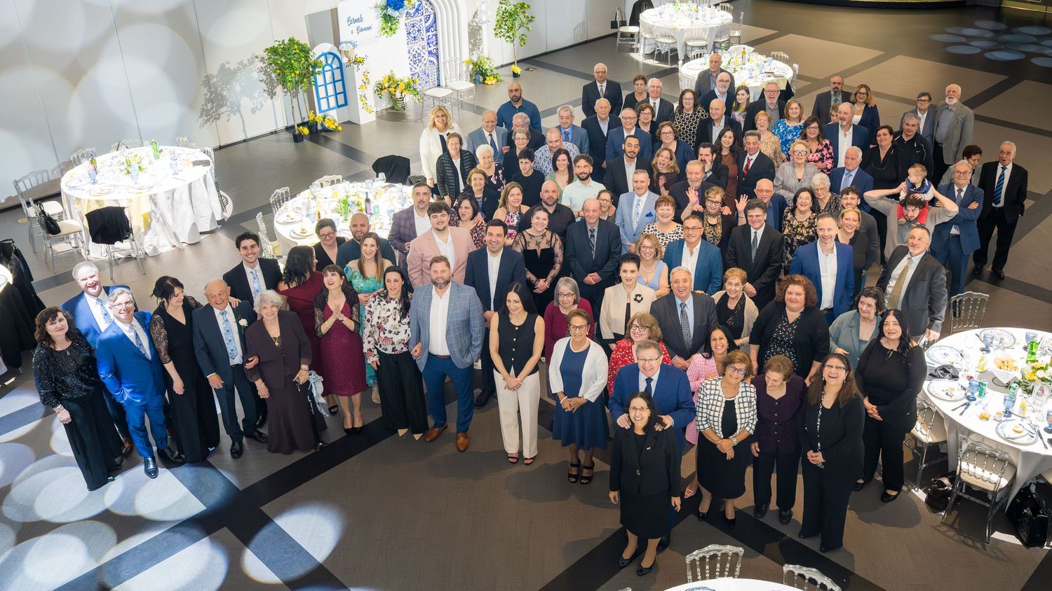 Large group photo of guests at a formal celebration event in a decorated banquet hall from above.