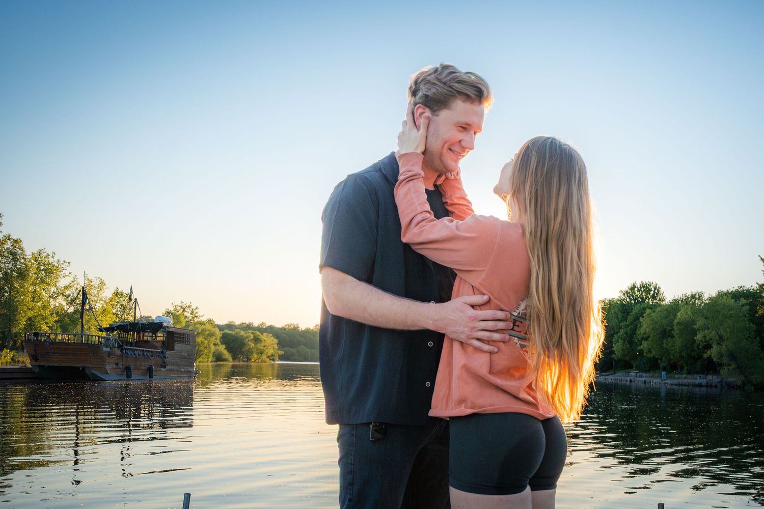 Happy couple embracing and smiling at each other by a beautiful lake at golden hour.