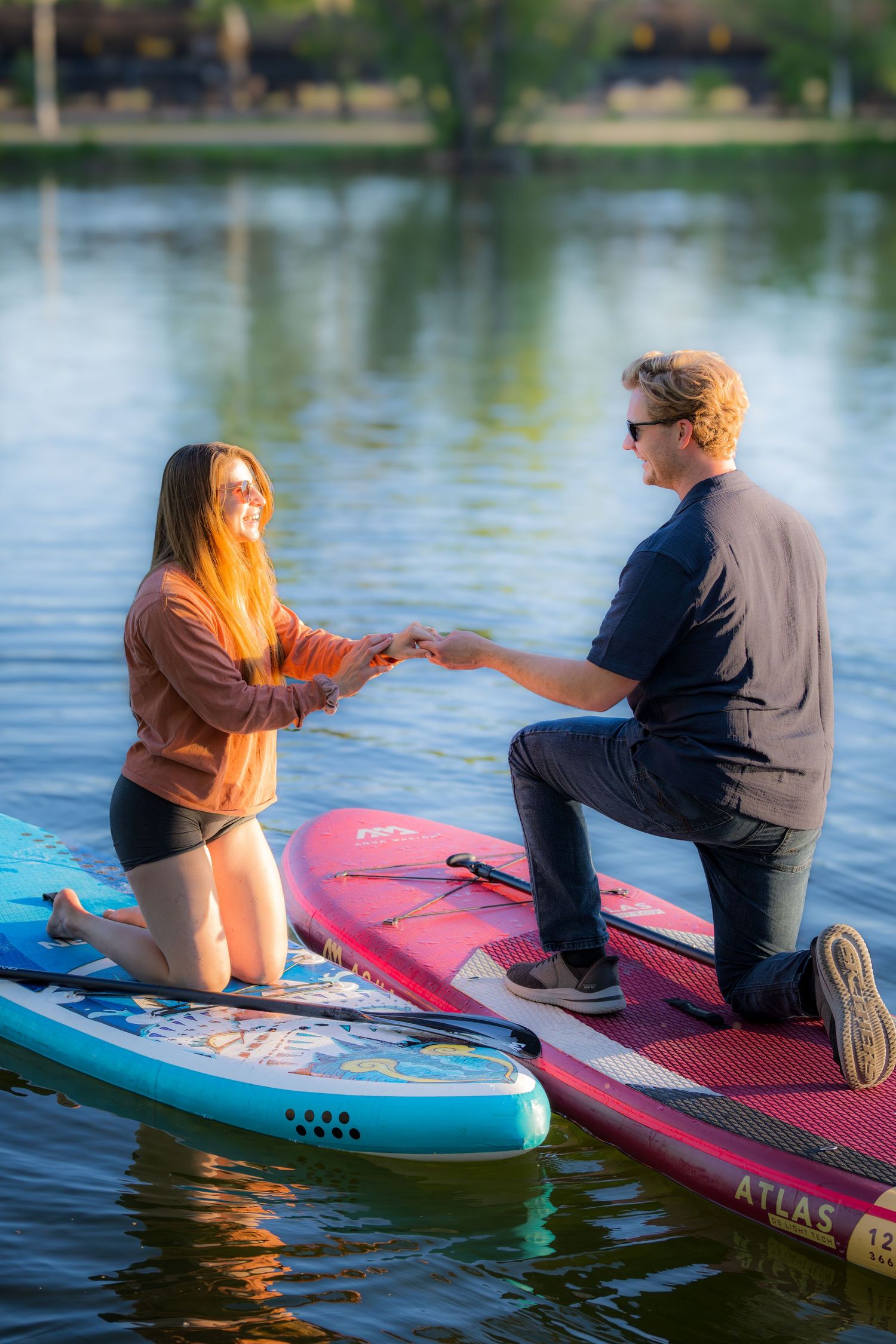 Man kneeling on a paddleboard proposing to a woman on the water during a sunny day.