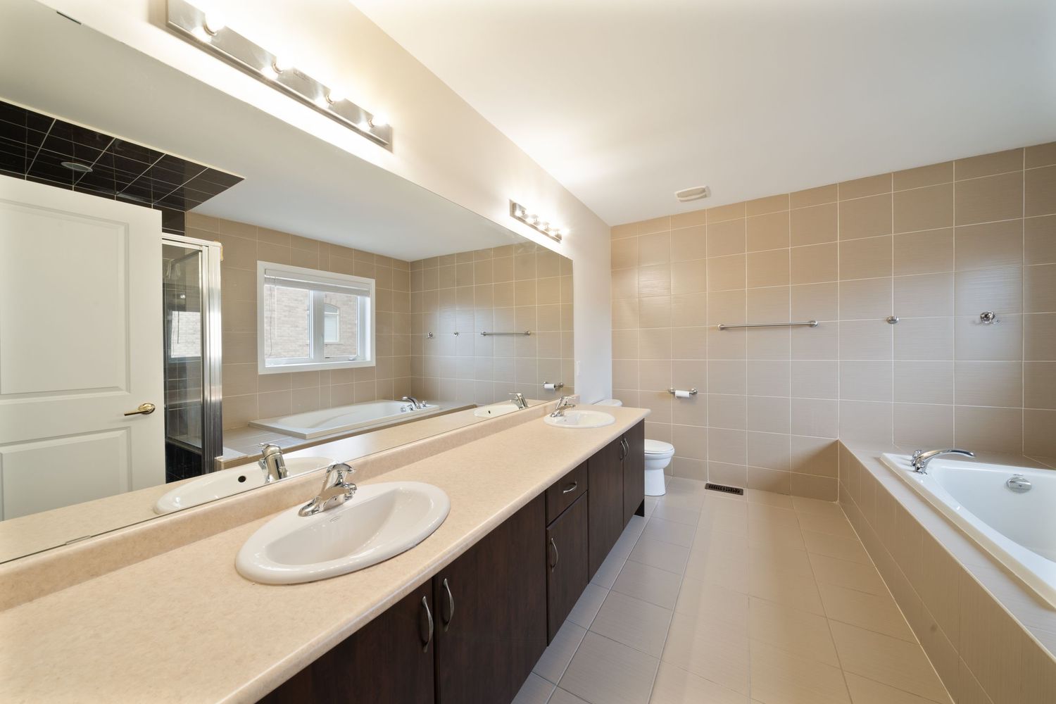 Modern bathroom interior with beige tiles, dark wood vanity, and white fixtures features clean lines and contemporary design.