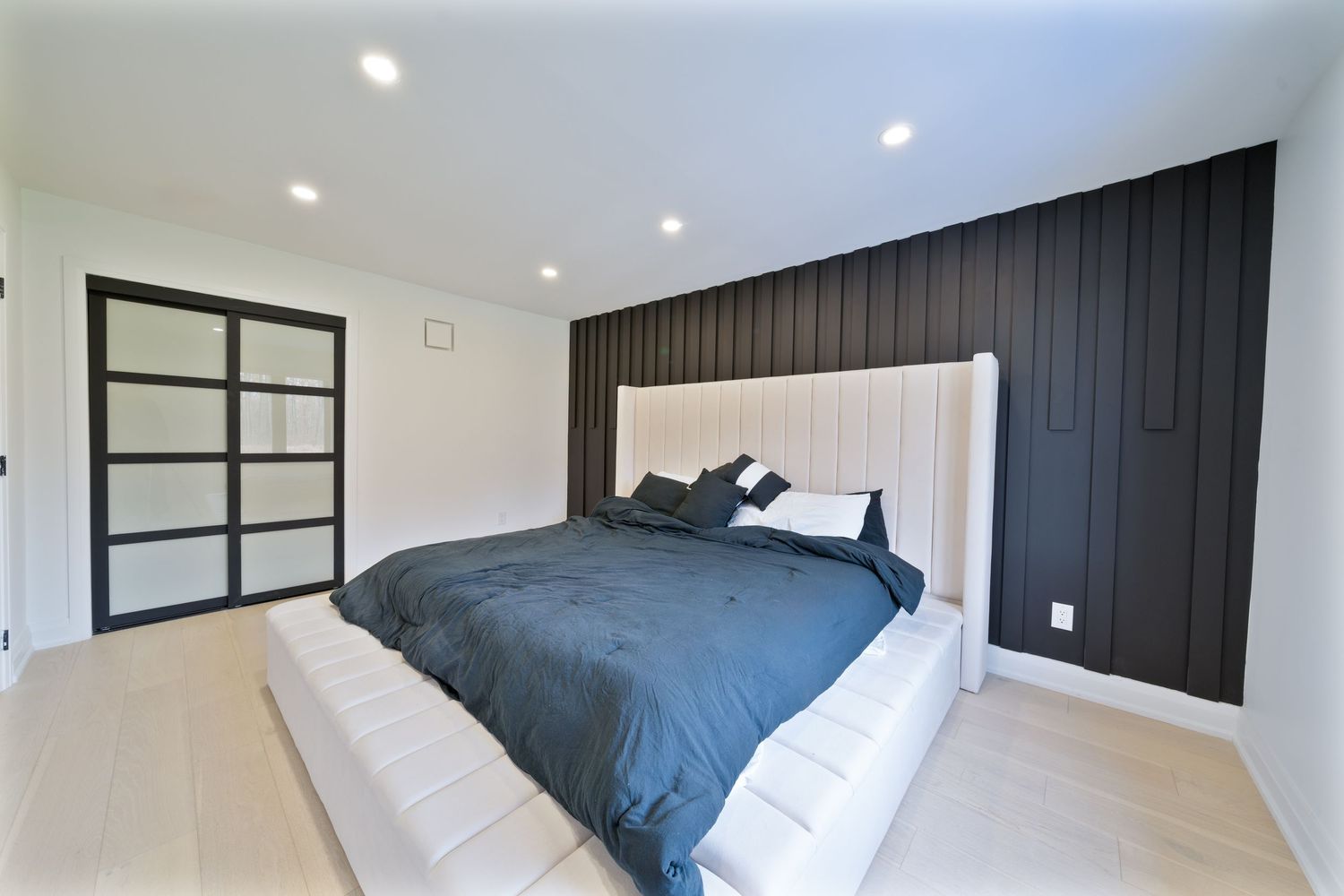 Minimalist bedroom featuring navy blue bedding, white walls, and built-in dark wood paneling details.