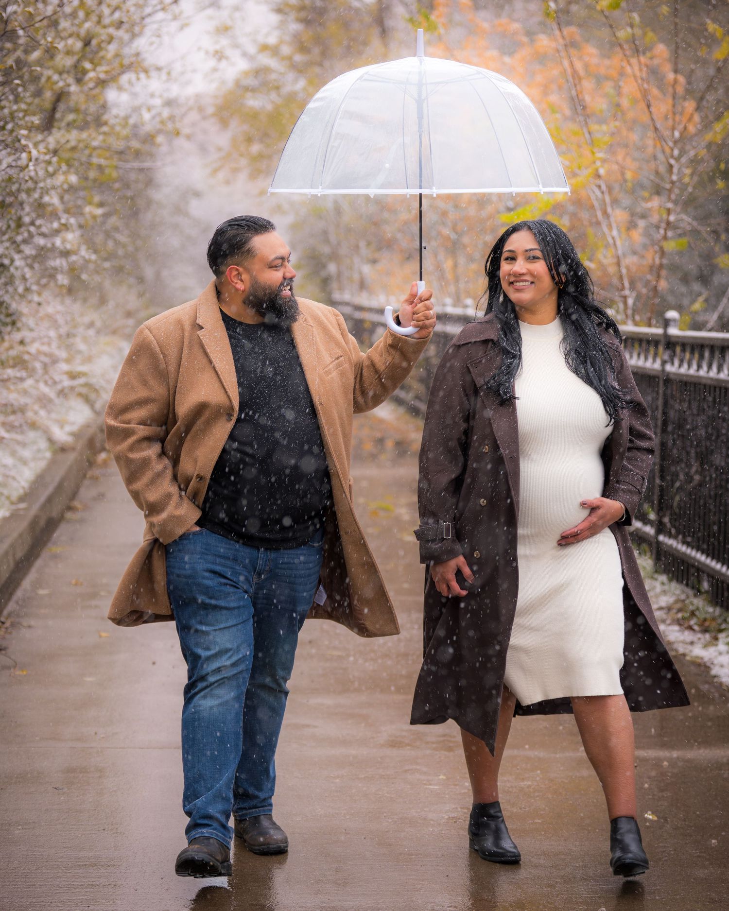 A couple shares a joyful moment walking in the snow under an umbrella.