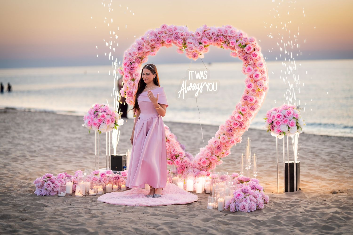 Beachside proposal scene with illuminated pink floral heart arch and decorative candles.