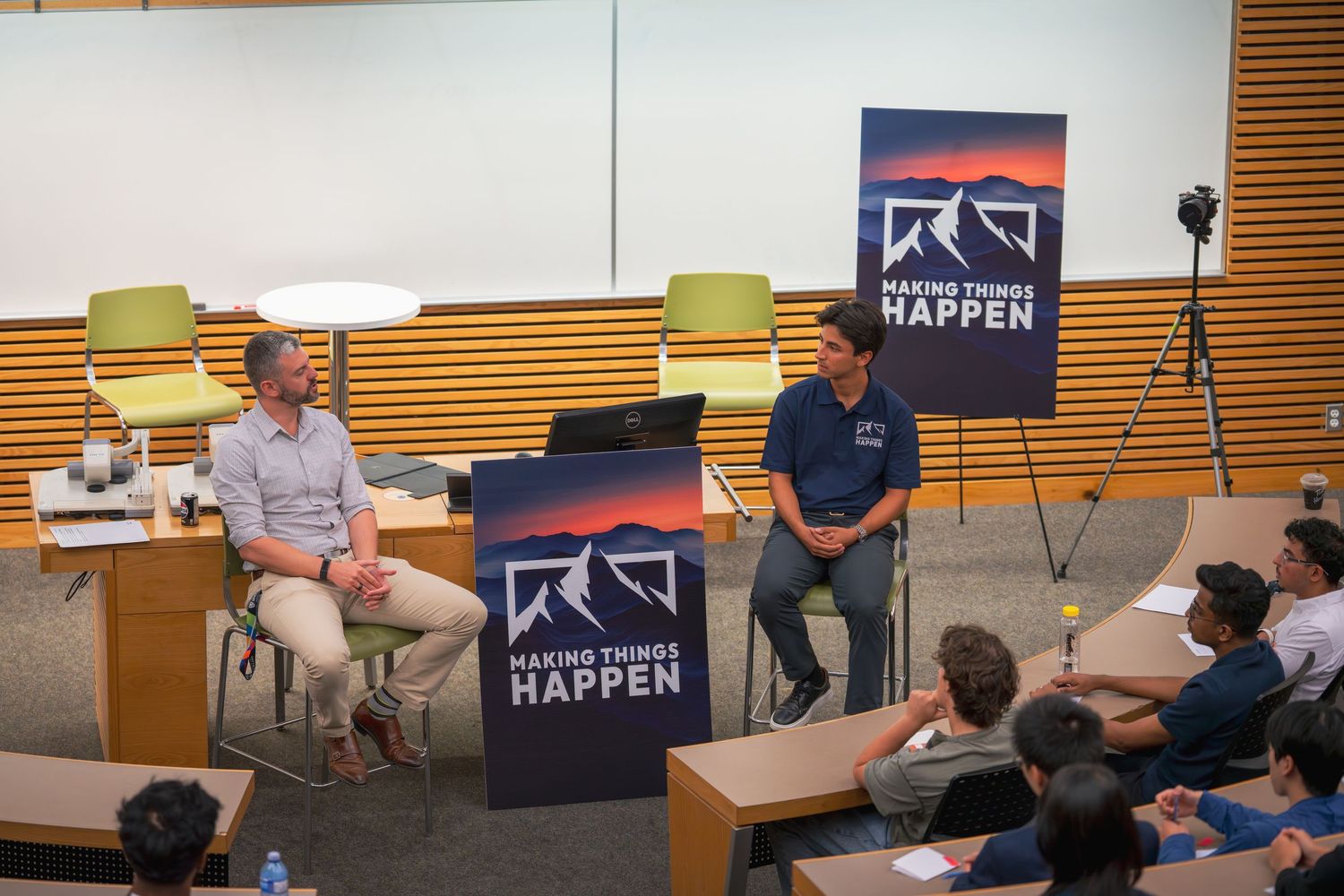 Audience members attending presentation in modern lecture hall with multiple display screens.