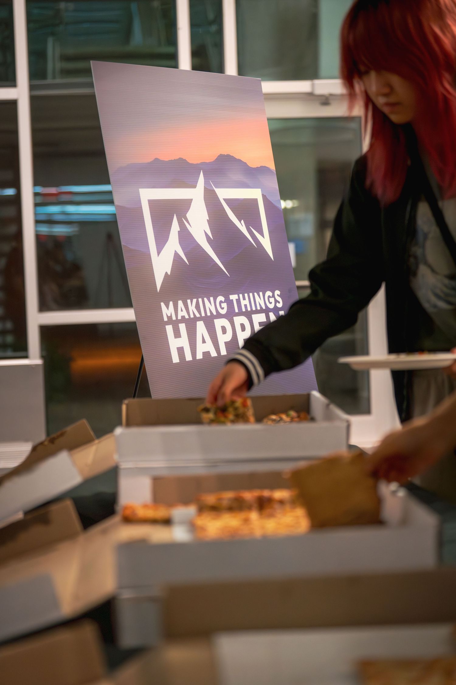 Pizza boxes and refreshments are served at a professional event with branded signage visible.