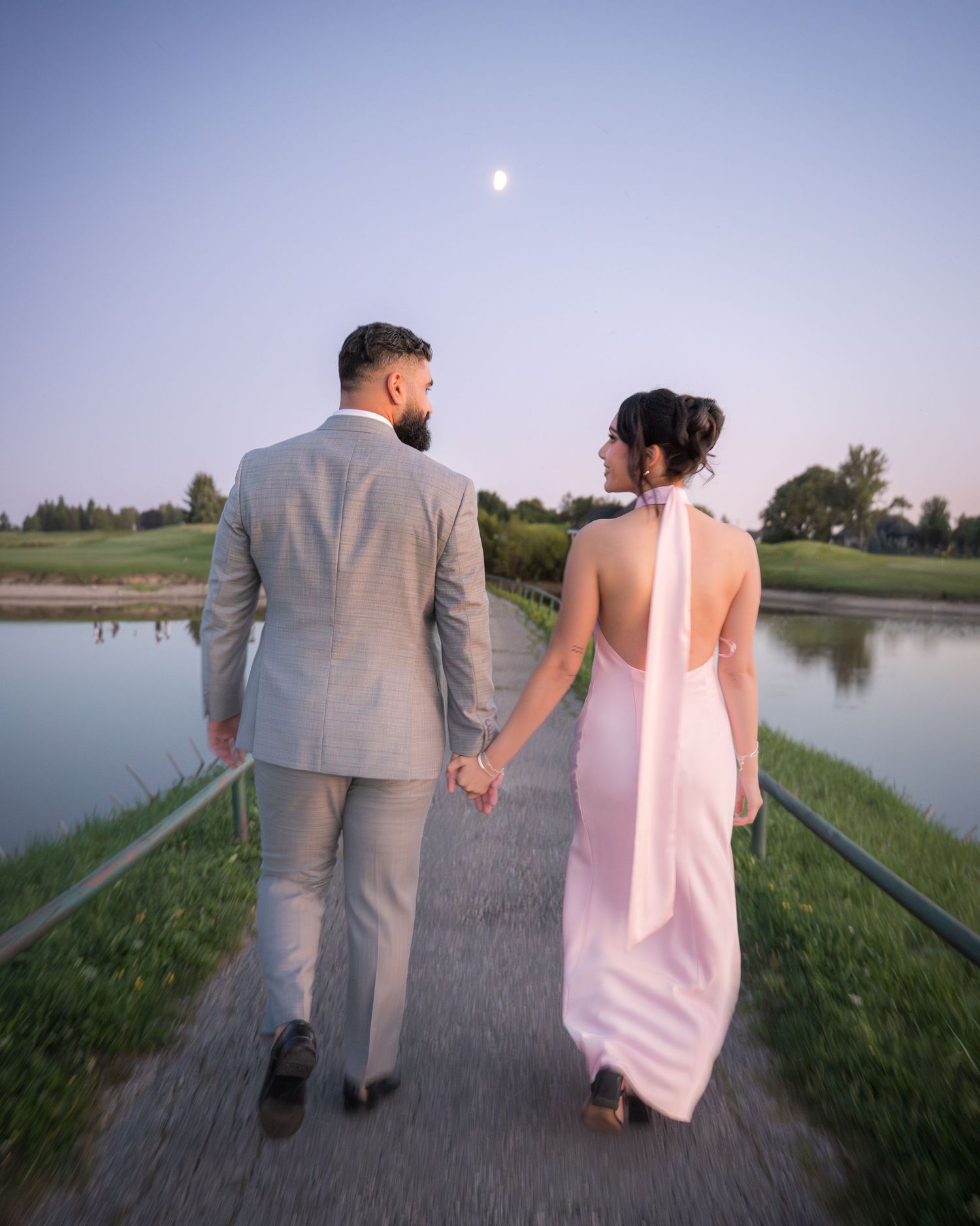 Couple strolls together on pathway beside scenic lake during sunset.