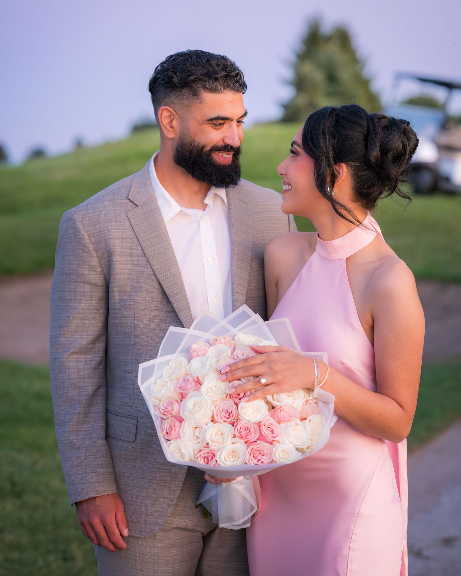 A couple gazes at each other while holding a romantic bouquet of pink and white roses.