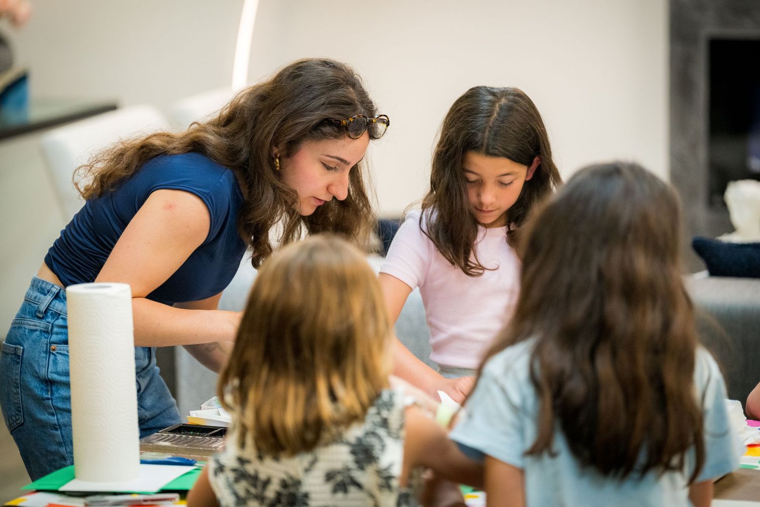 Woman and three girls engaged in a creative art activity together at a colorful table indoors.