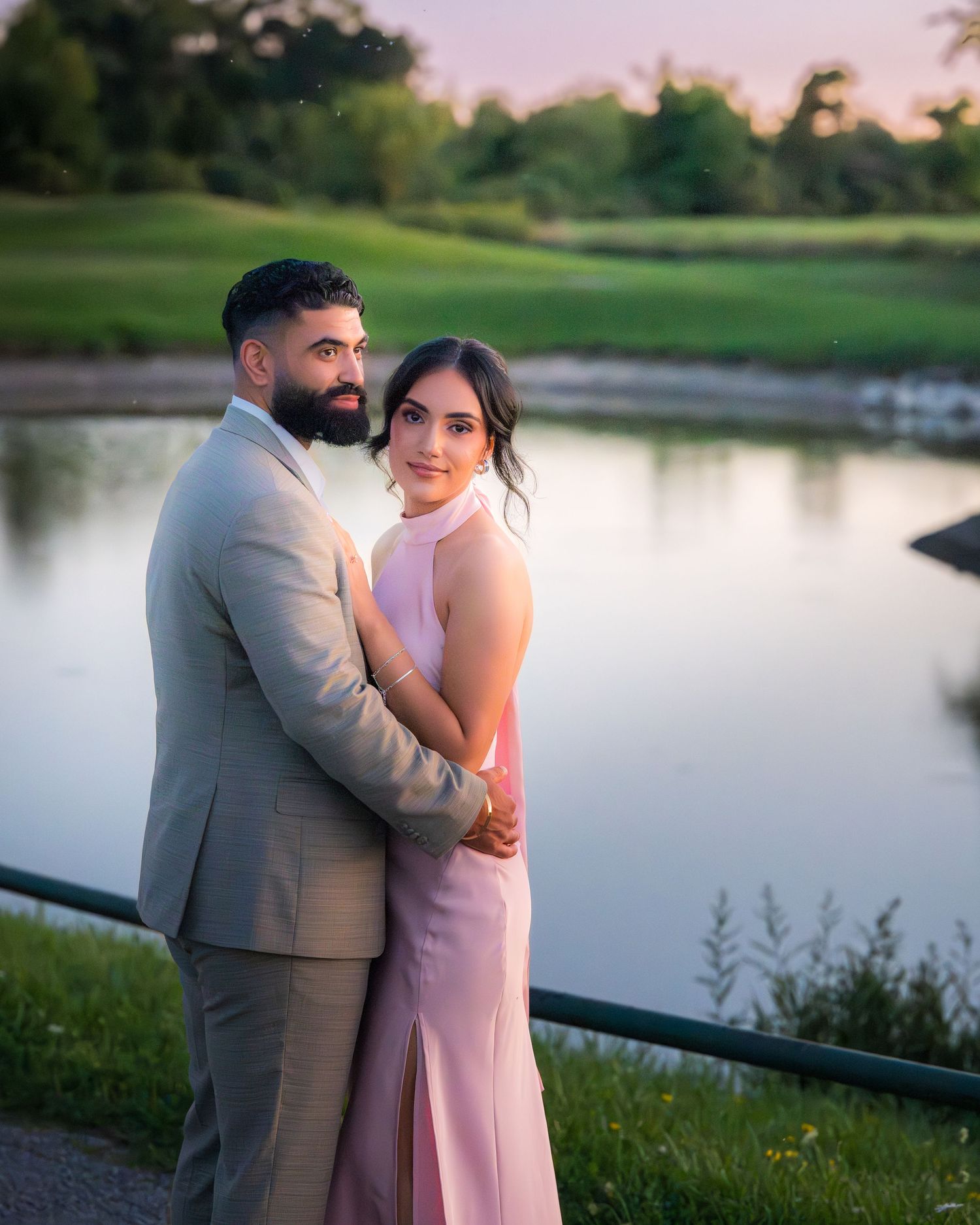 Romantic sunset portraits of couple by lake in pink dress and grey suit.