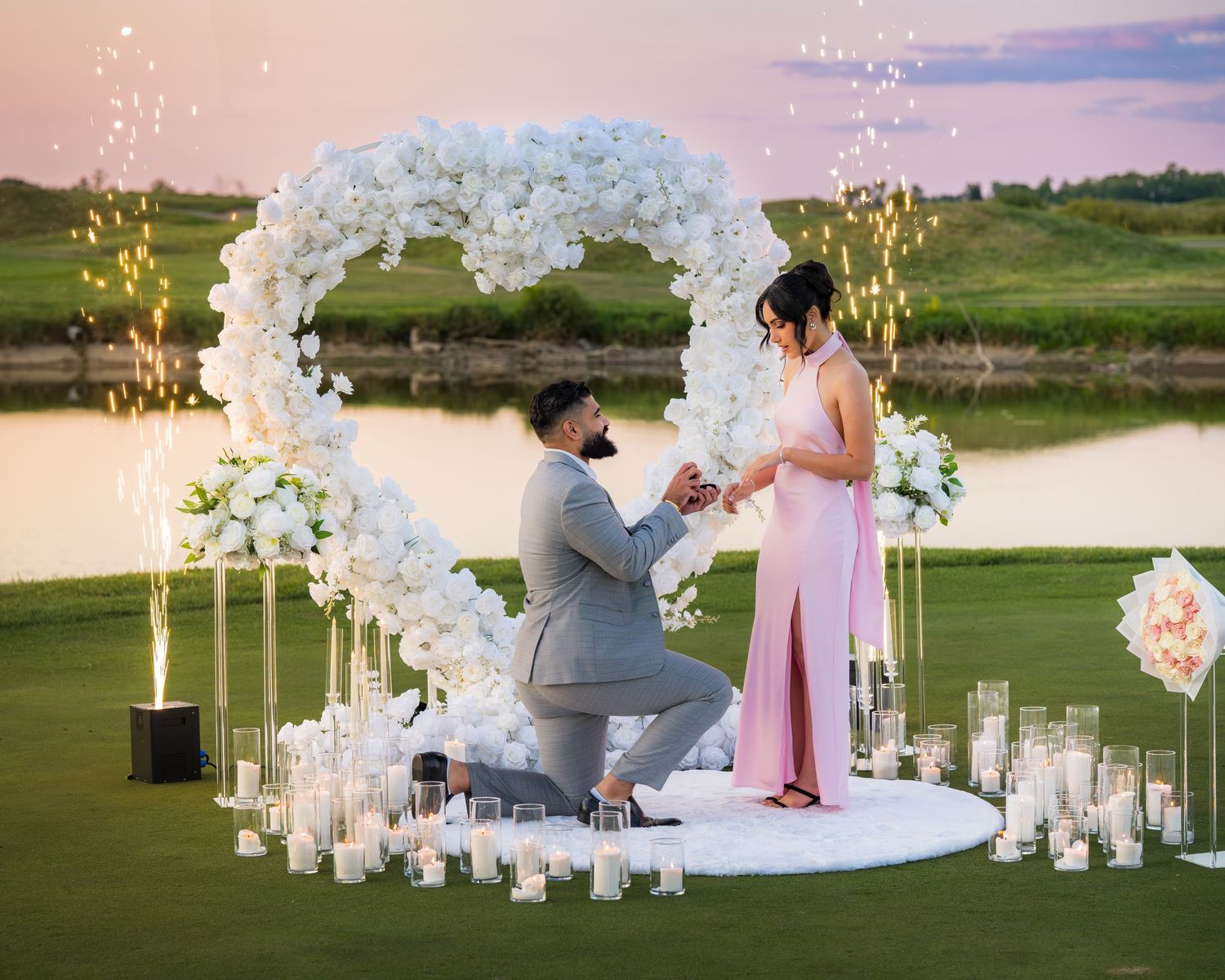 Sunset proposal with elegant white floral arch and candlelit decorations.