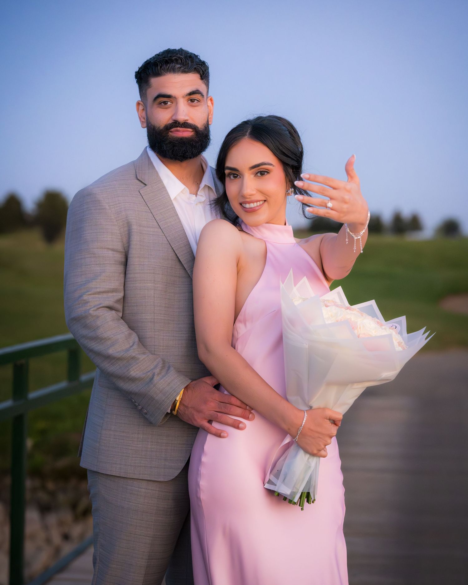 A couple poses with a white bouquet during their sunset photoshoot by a lake.