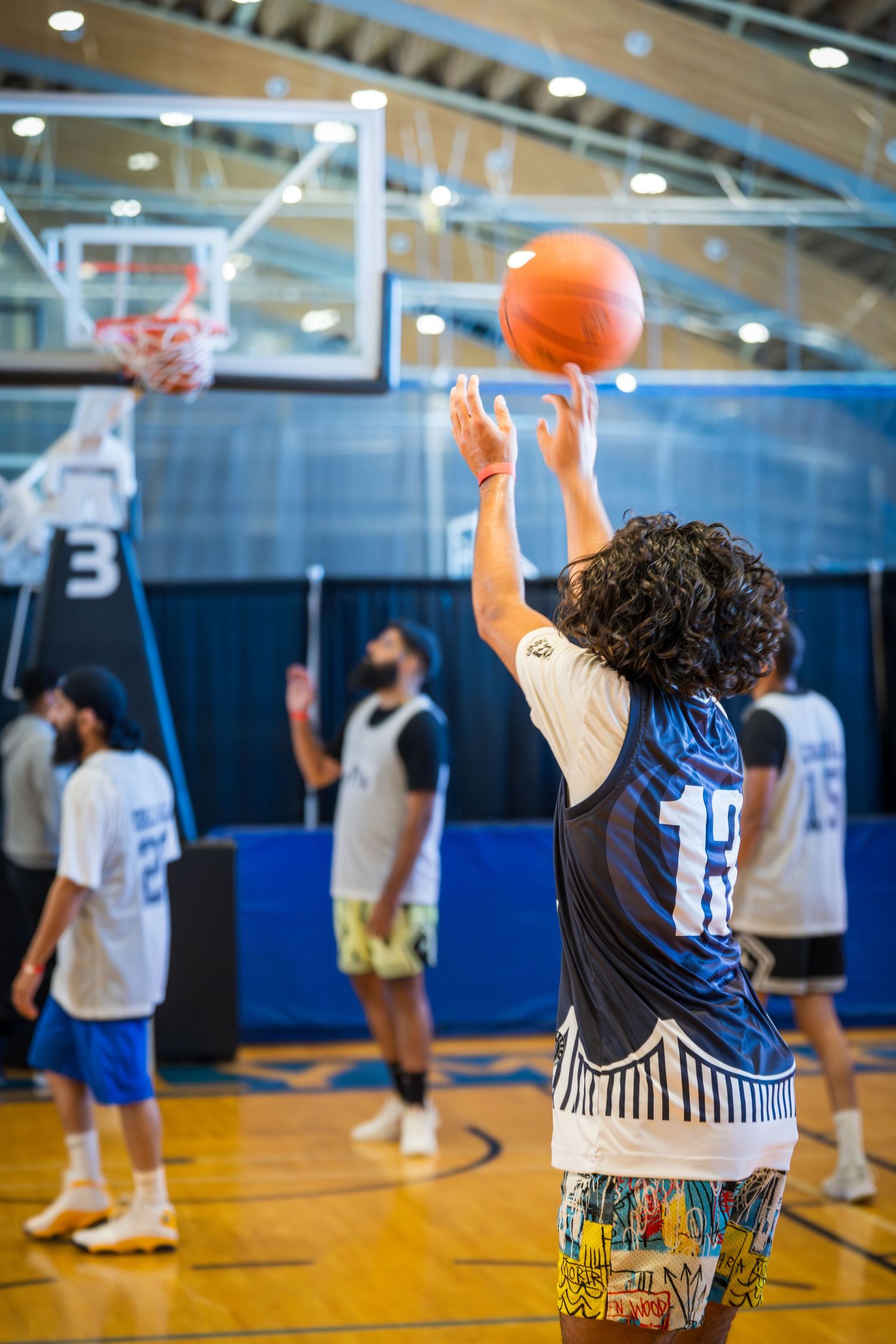 Basketball players practice shooting drills in a gymnasium with blue walls and hardwood floors.