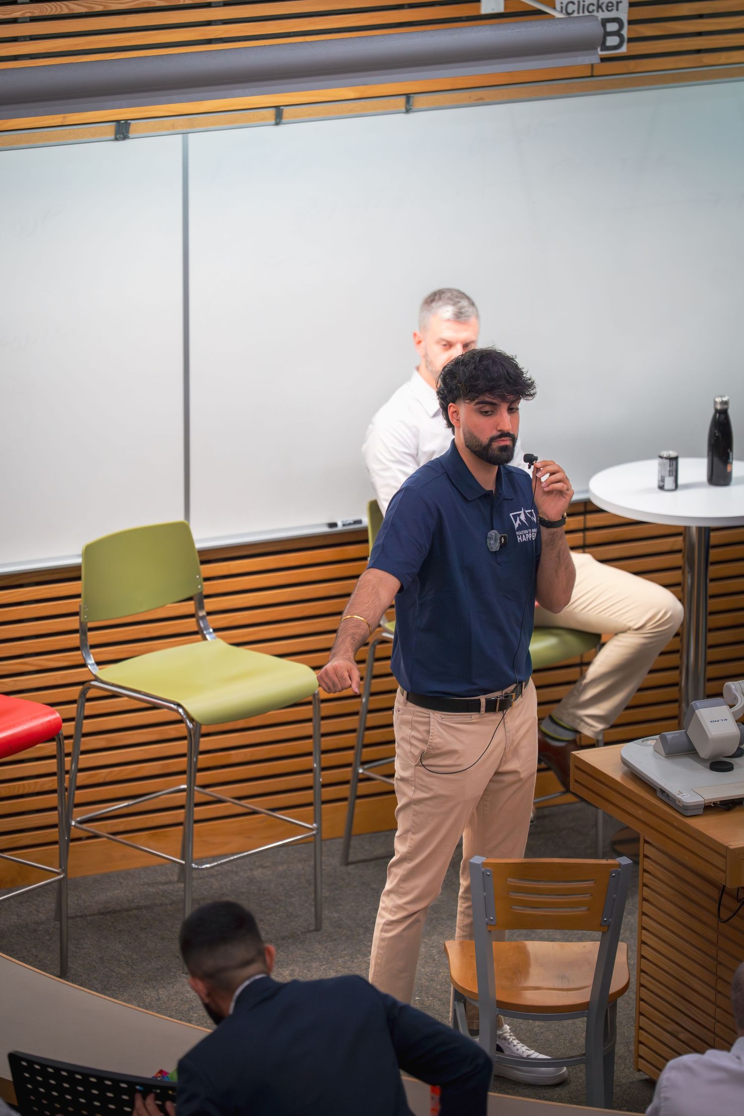 Speaker addresses audience while standing in front of colorful chairs in a conference room.
