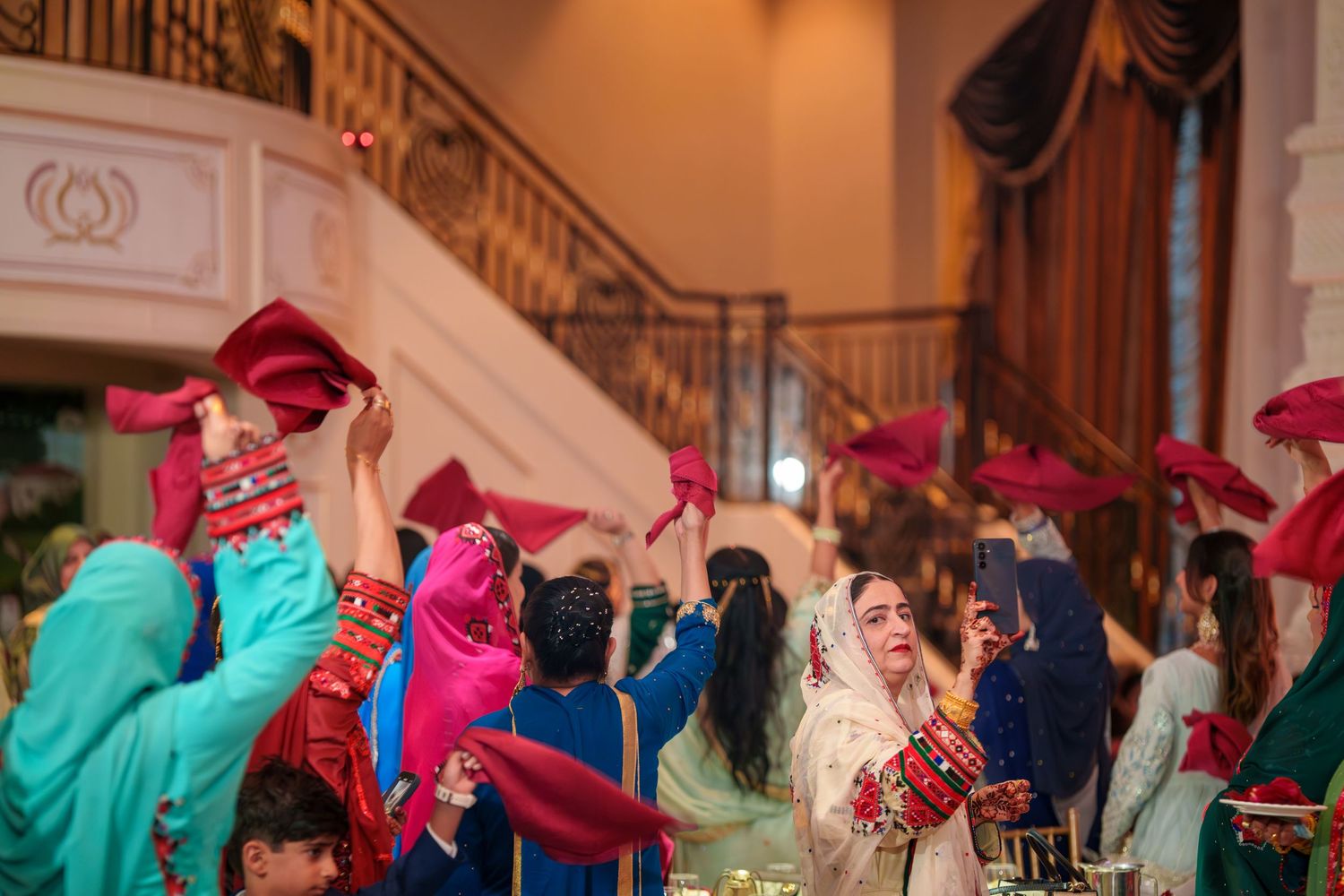 Wedding celebration scene with guests in colorful attire taking photos at reception venue.