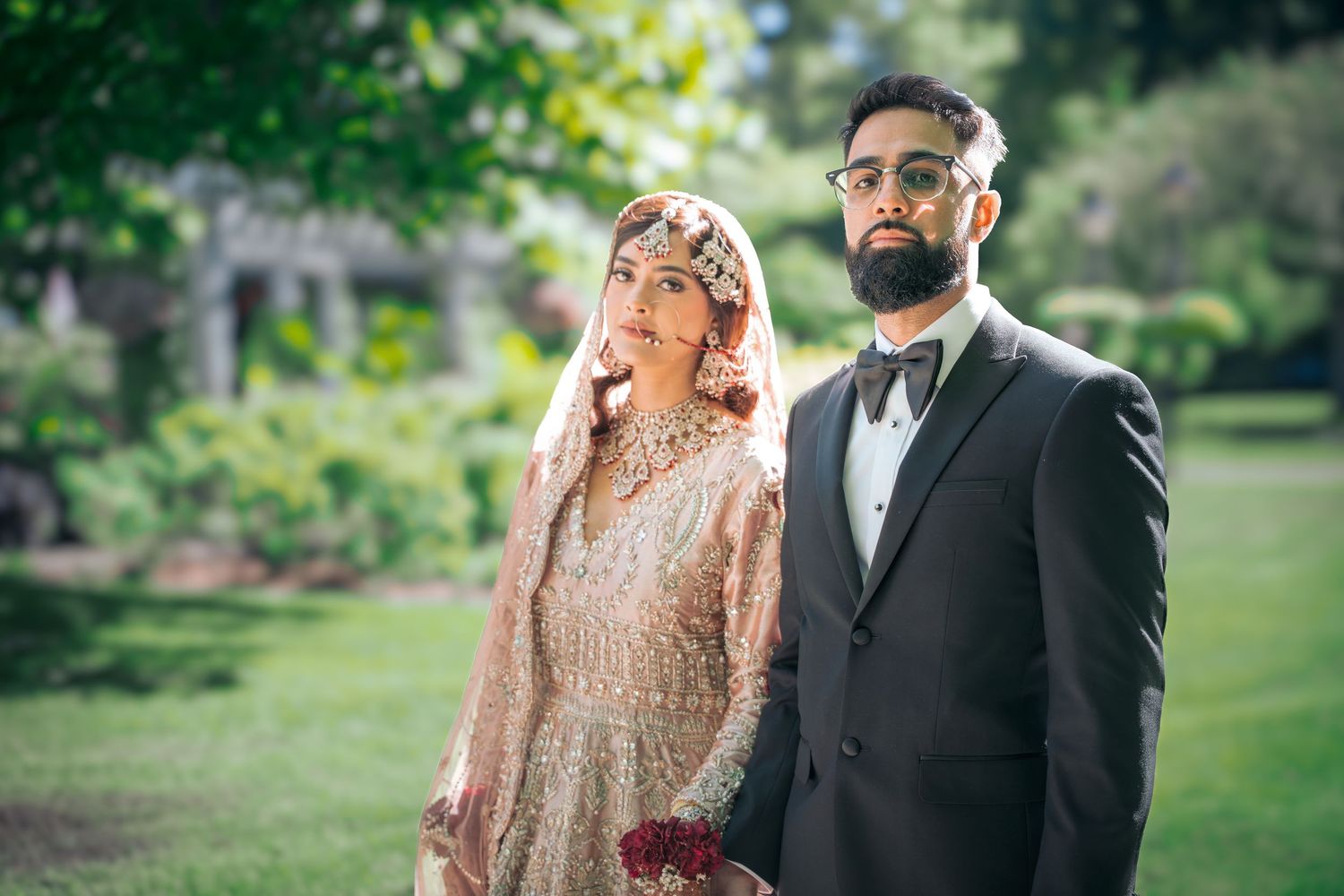 Wedding couple stands together in an outdoor garden setting with vibrant green landscaping.
