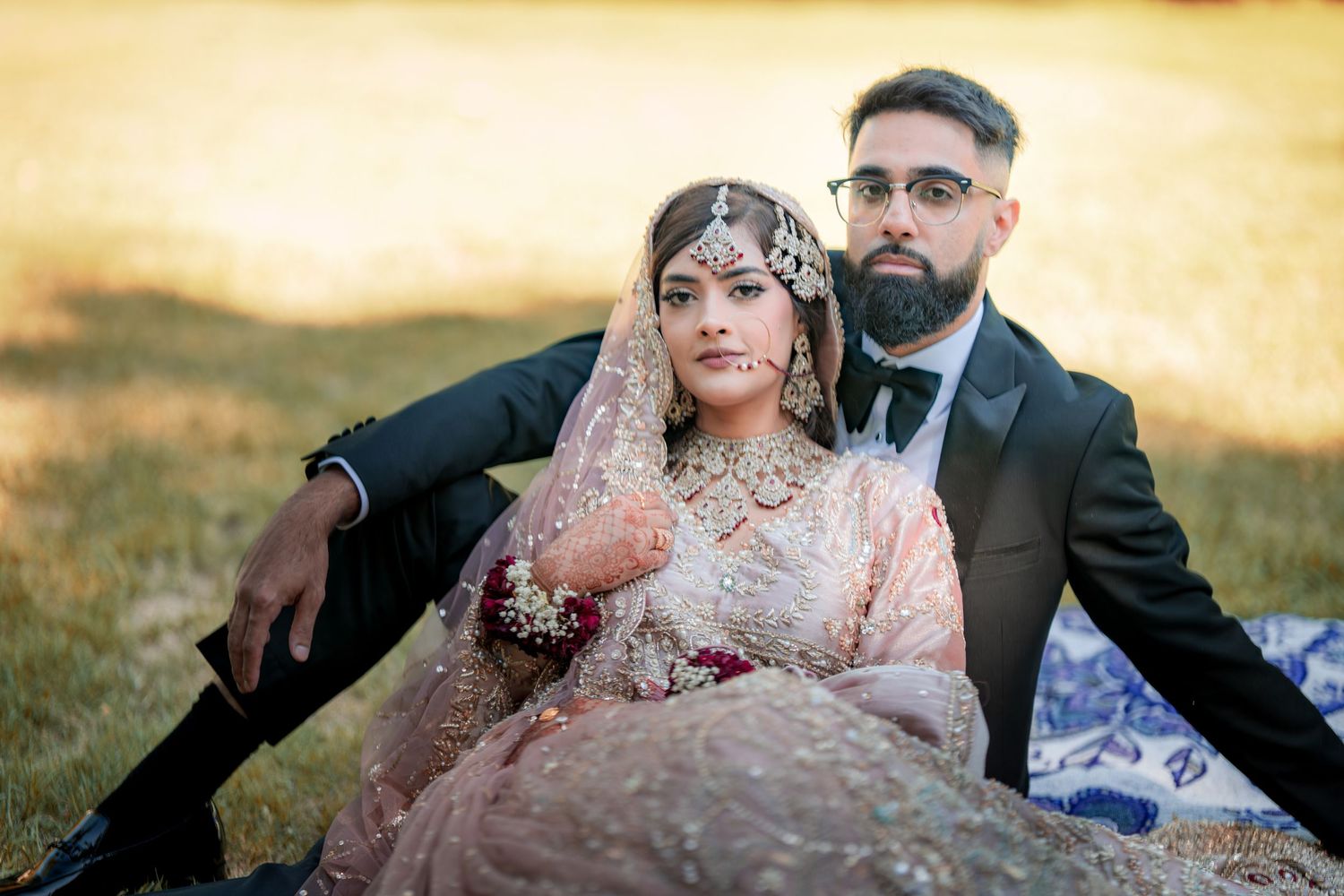 Wedding couple in traditional South Asian formal wear poses outdoors during sunset.