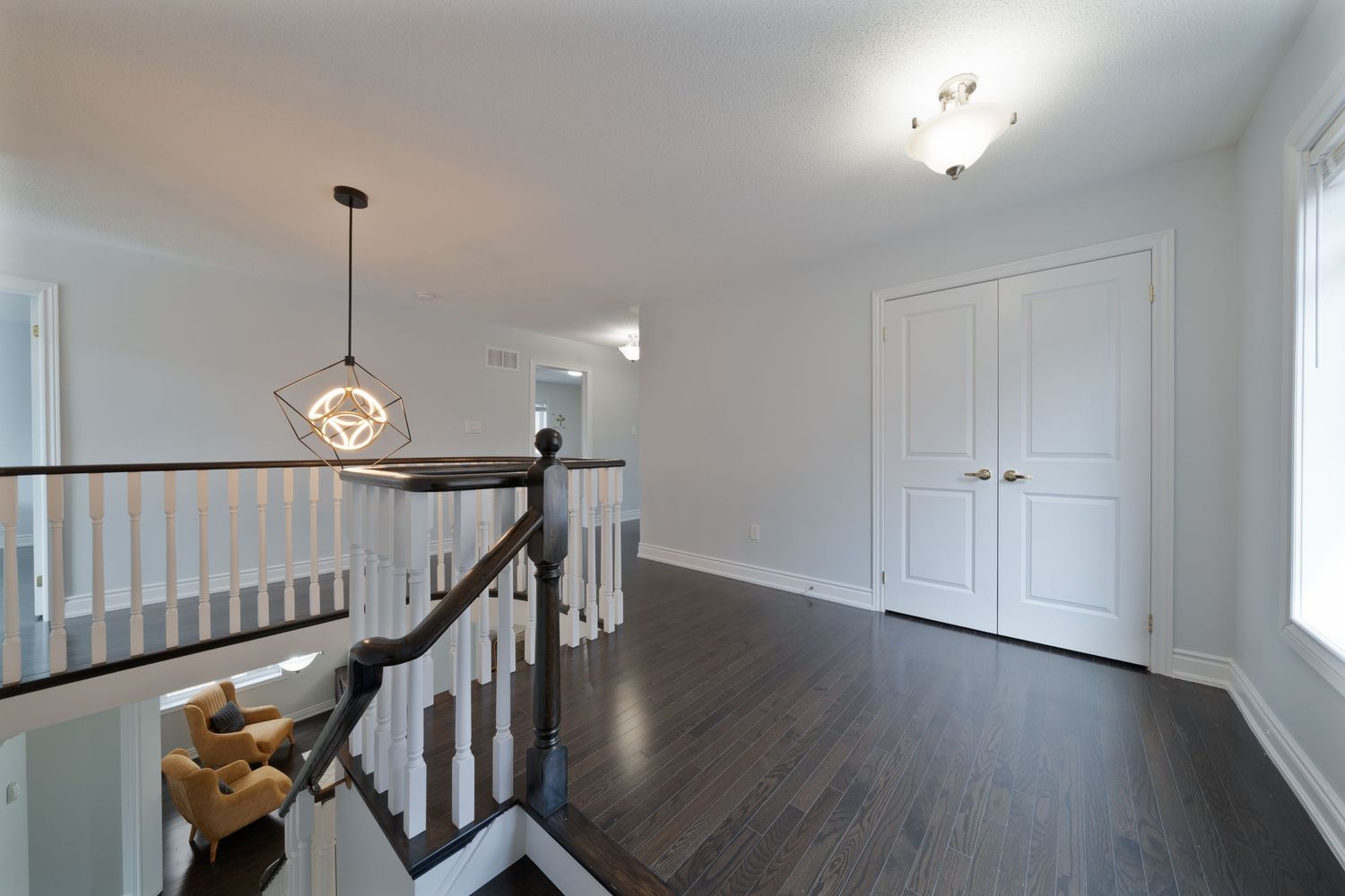 Modern white kitchen with dark hardwood floors features a center island, pendant lights, and stainless steel appliances.