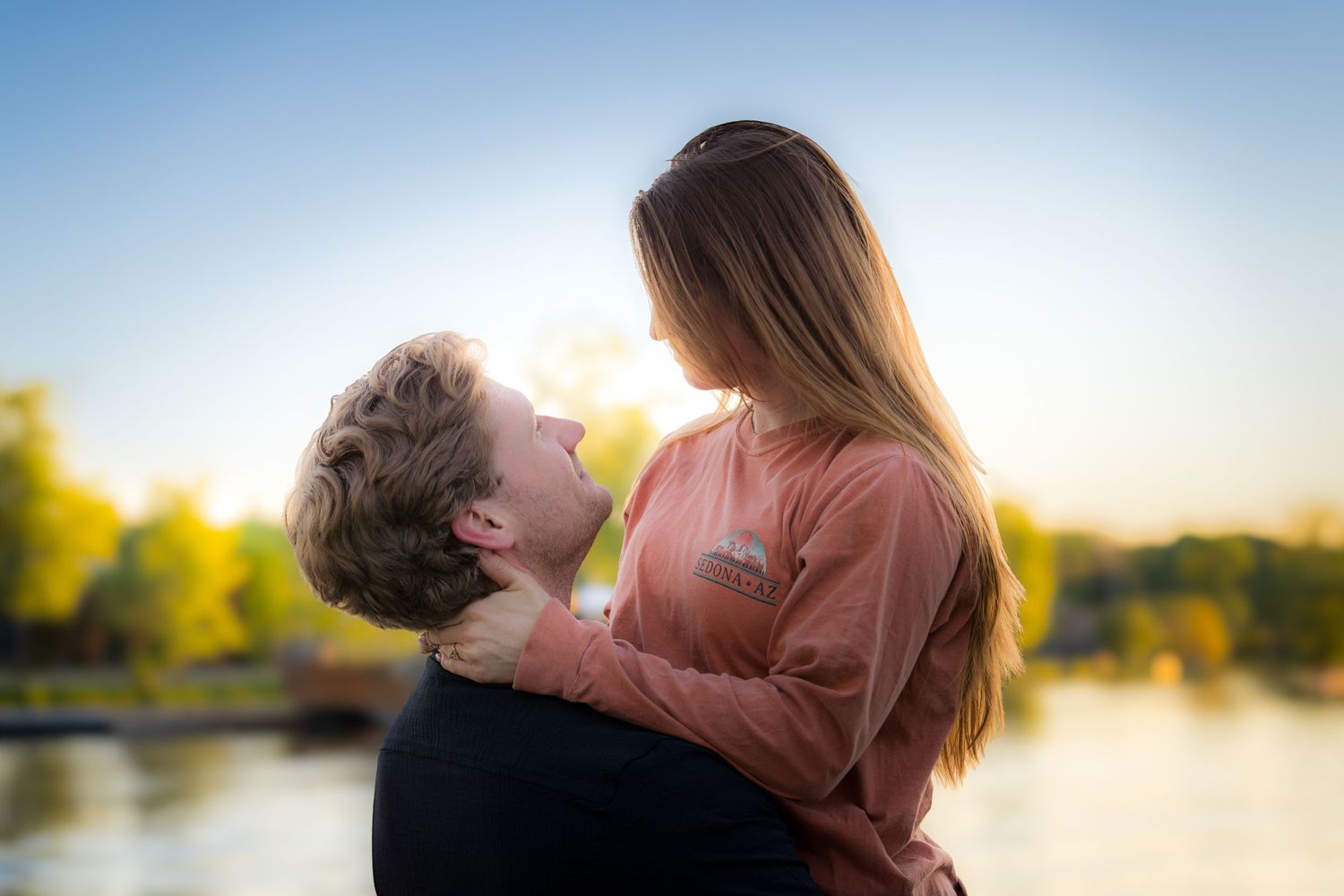 Romantic couple holding each other close near a lake during a golden sunset.