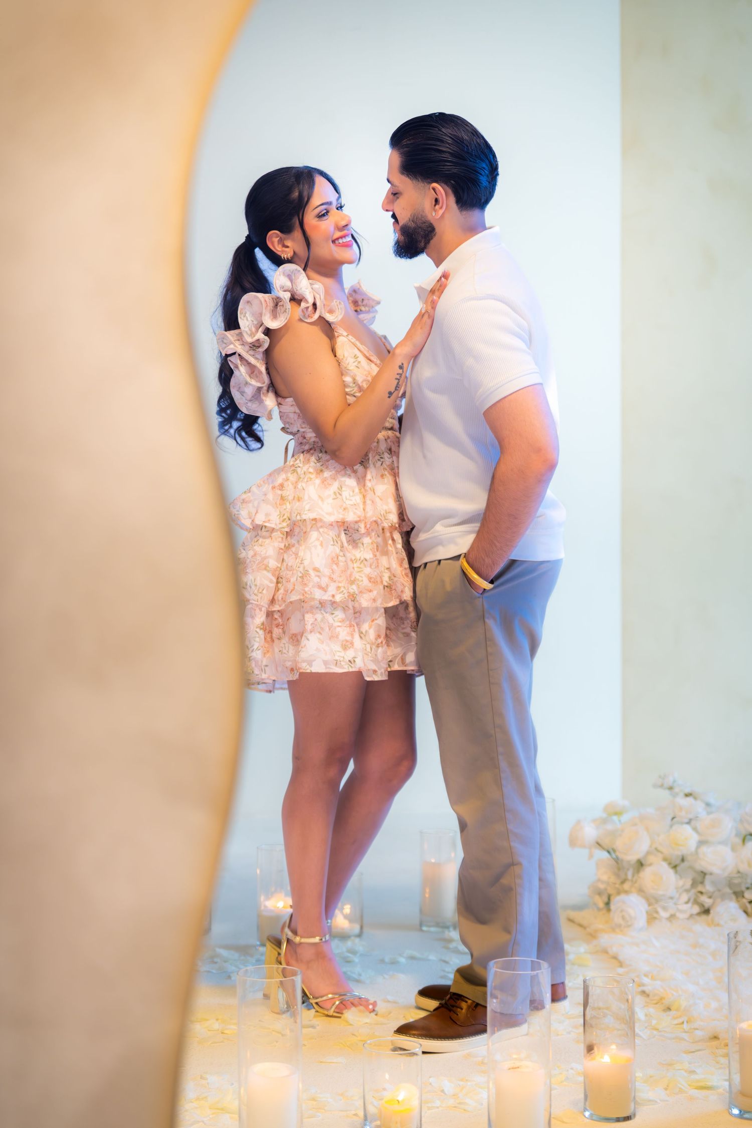 Happy couple embracing and smiling at each other surrounded by candles and white floral decor.