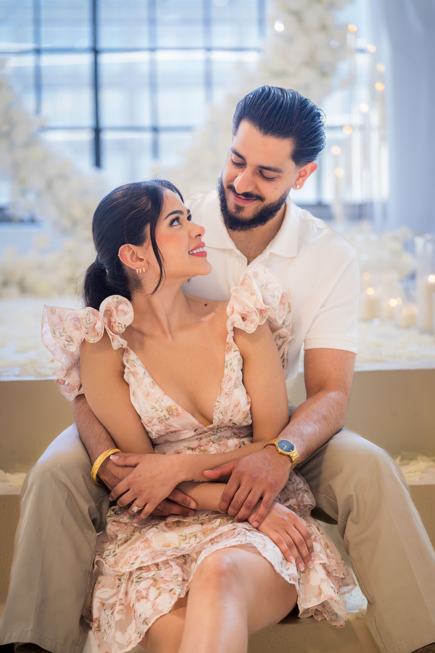 Couple sharing a romantic moment seated together in an elegantly decorated white floral venue.