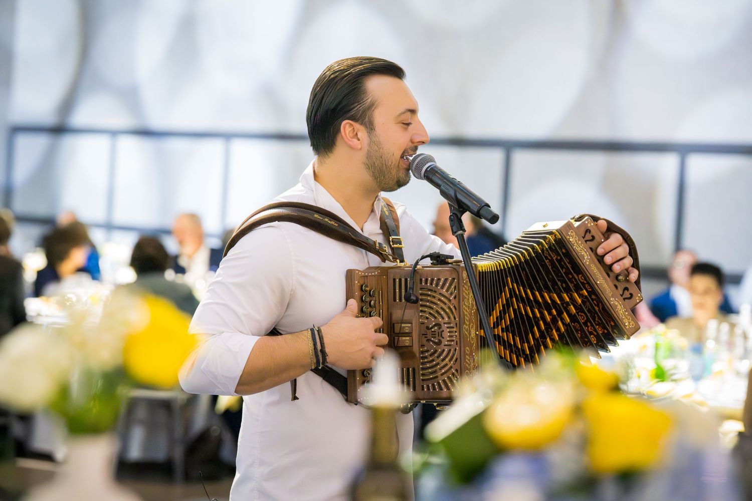 Male accordion player singing passionately into microphone at elegant yellow and white floral reception event.
