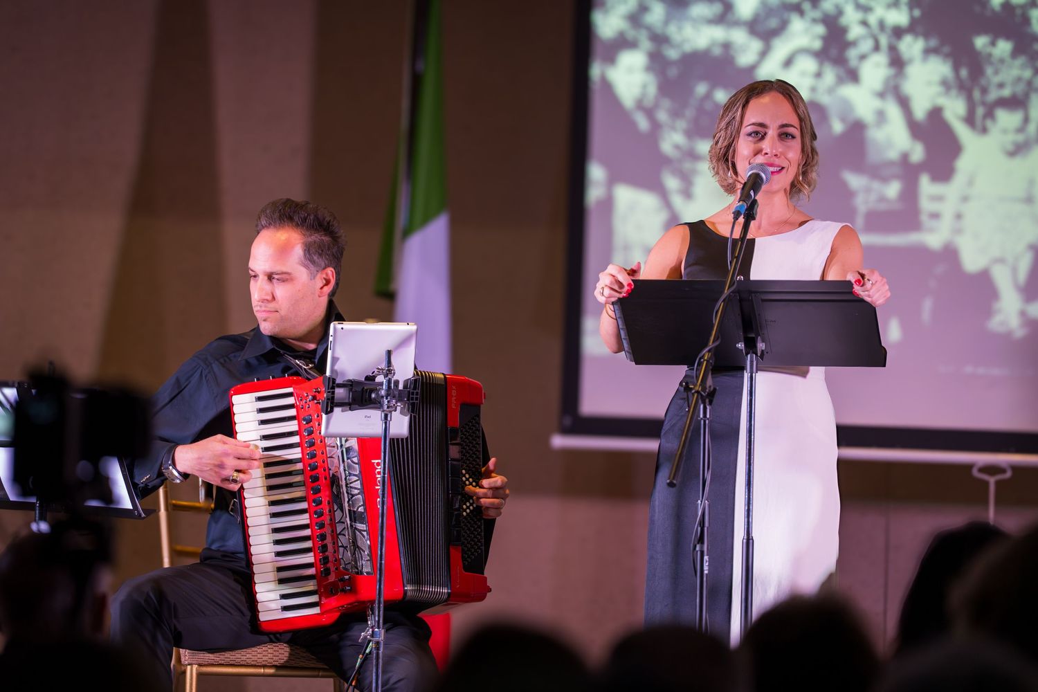 A male accordionist and a female vocalist perform together on stage at an Italian cultural music event.