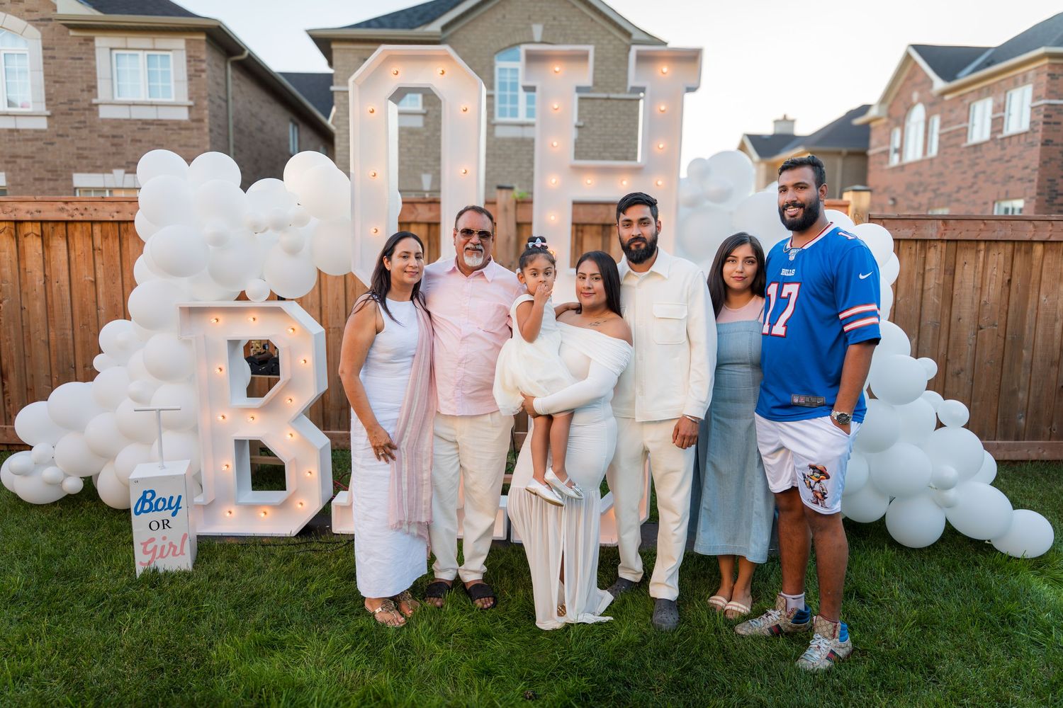 Family group poses in front of lit BOY OR GIRL gender reveal backdrop with balloon arch.