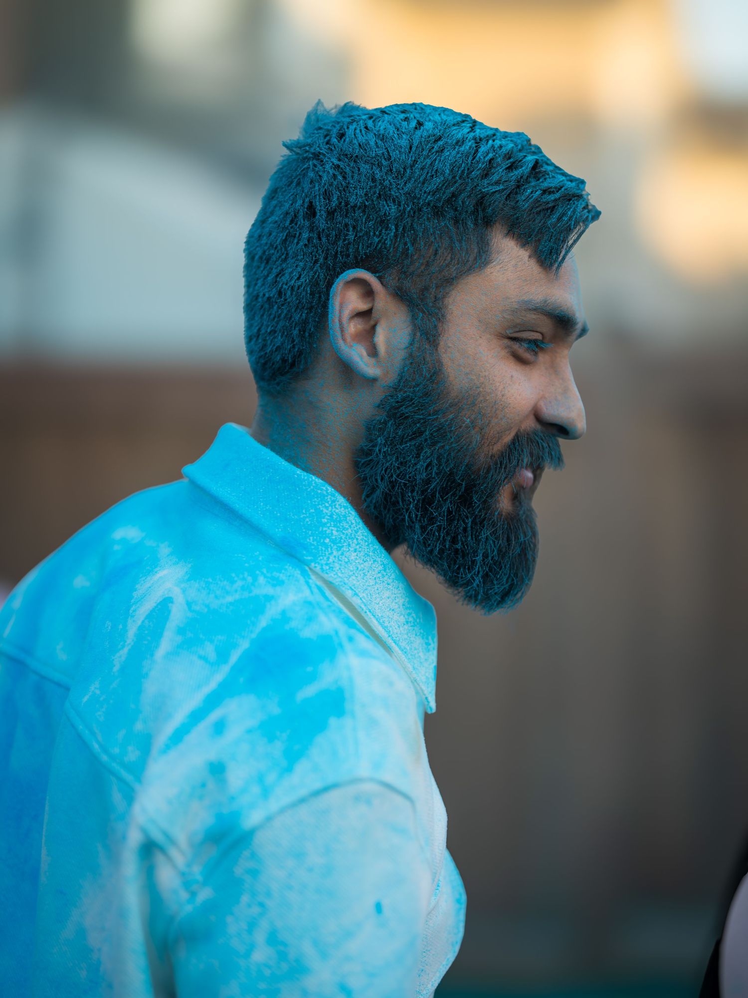 Man with blue powder in his beard and hair smiling during Holi festival celebration outdoors.