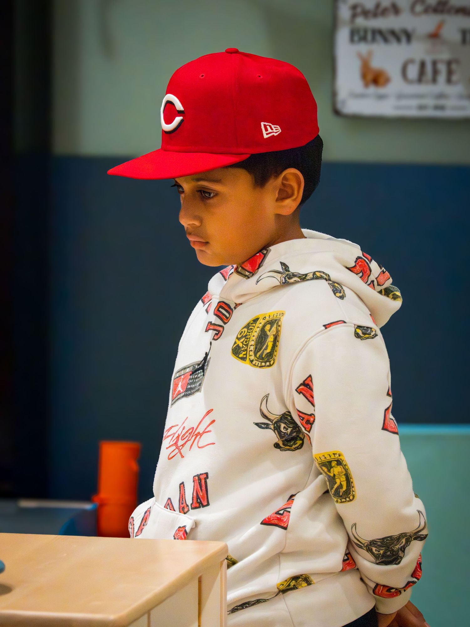 Young boy wearing a red Cincinnati Reds cap and graphic hoodie at a play cafe.