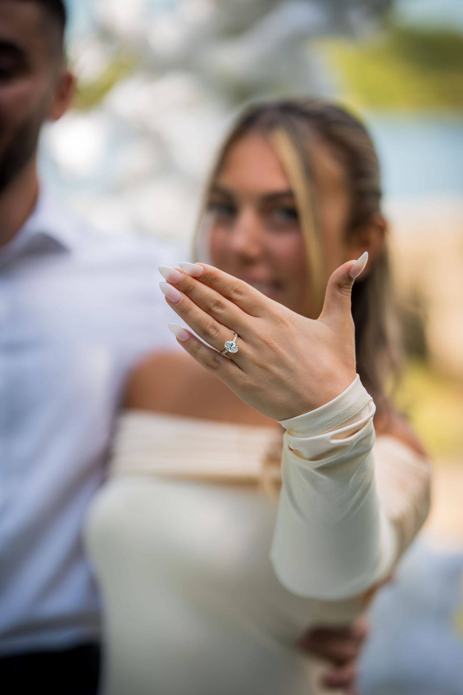 Close-up of an engagement ring on hand with white sleeve against blurred background.